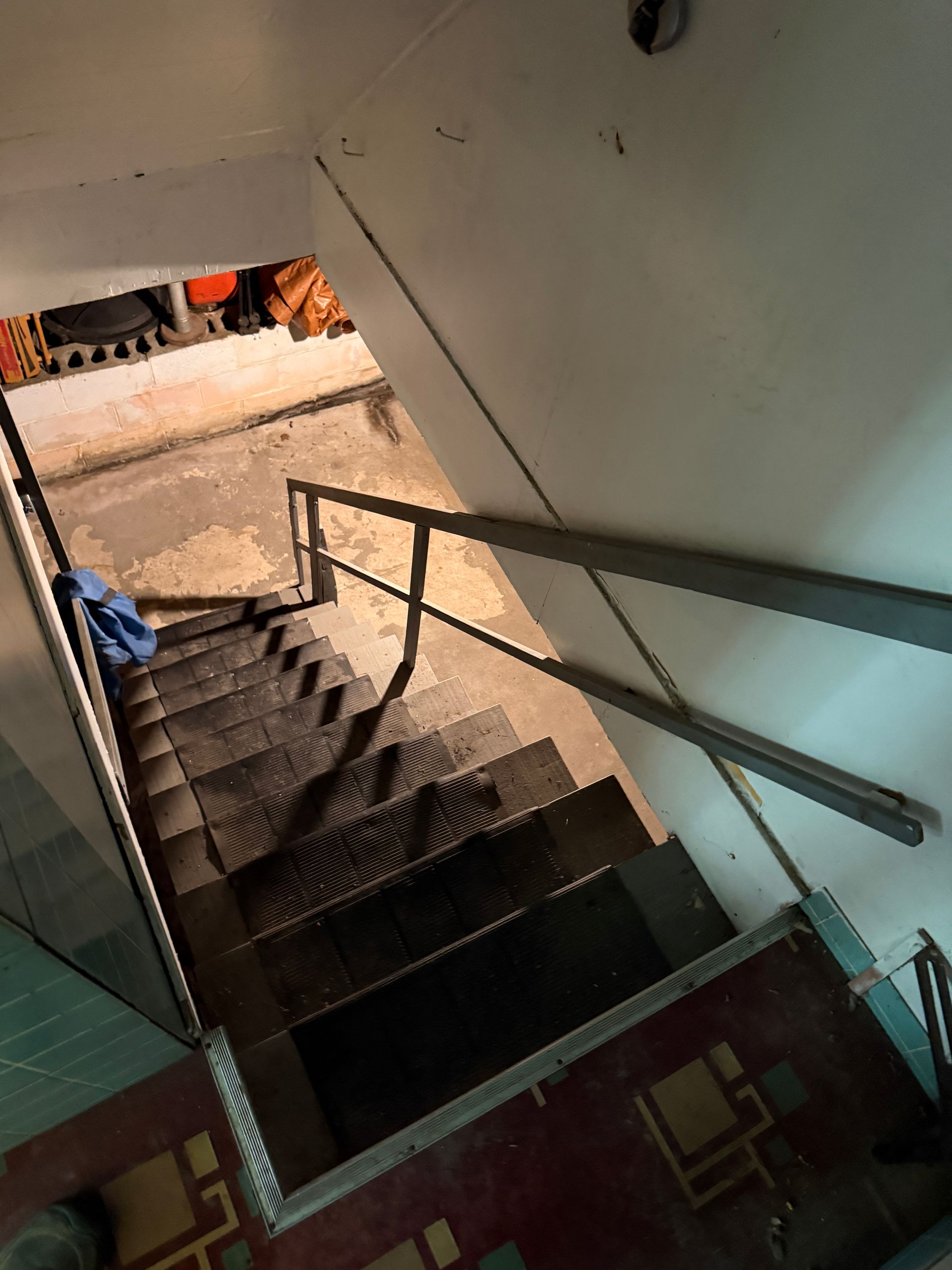 Stairwell with metal handrails leading down to a basement landing and open doorway