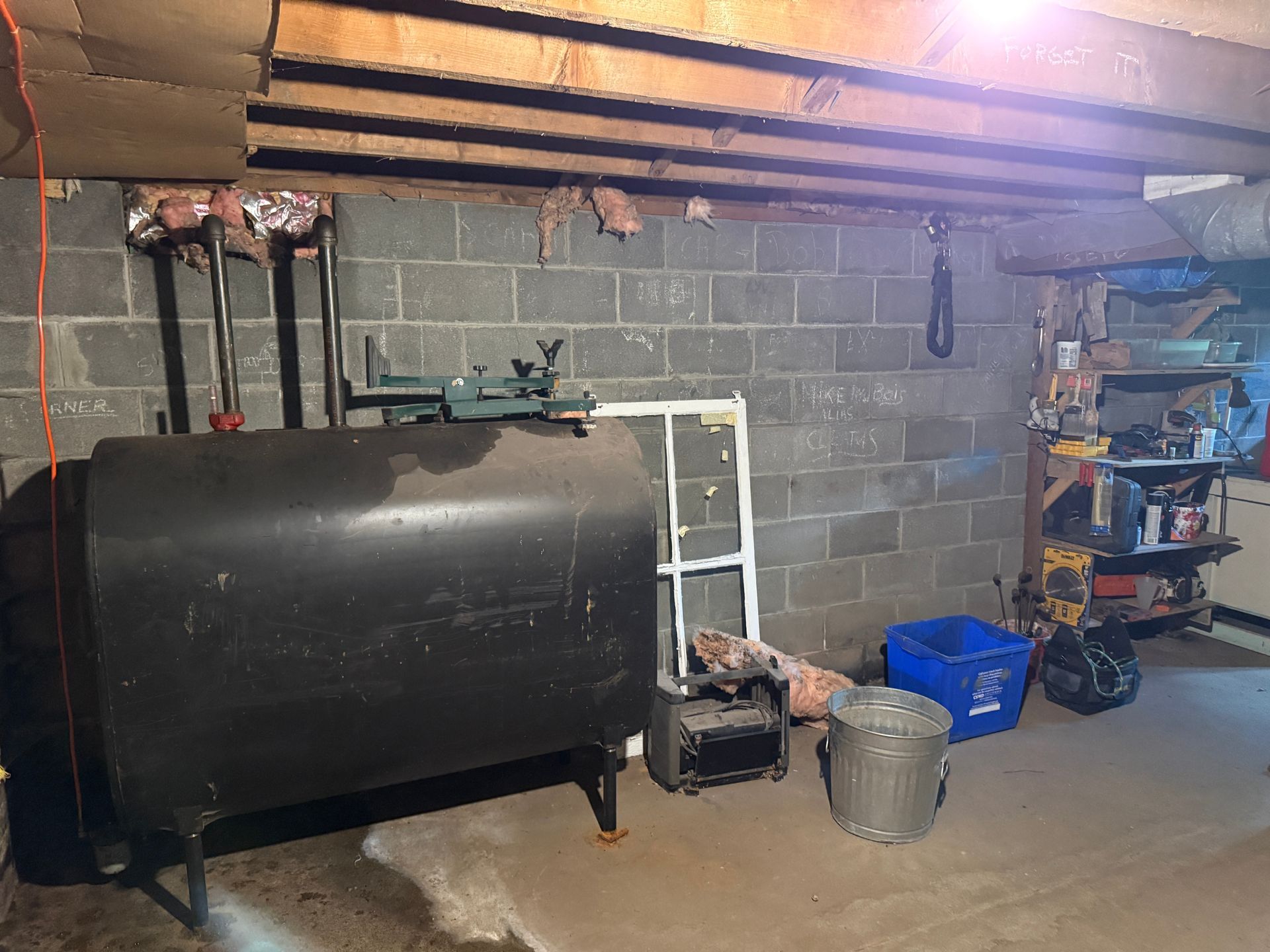 Basement with black fuel tank, cinder block walls, shelves, and storage bins under exposed joists
