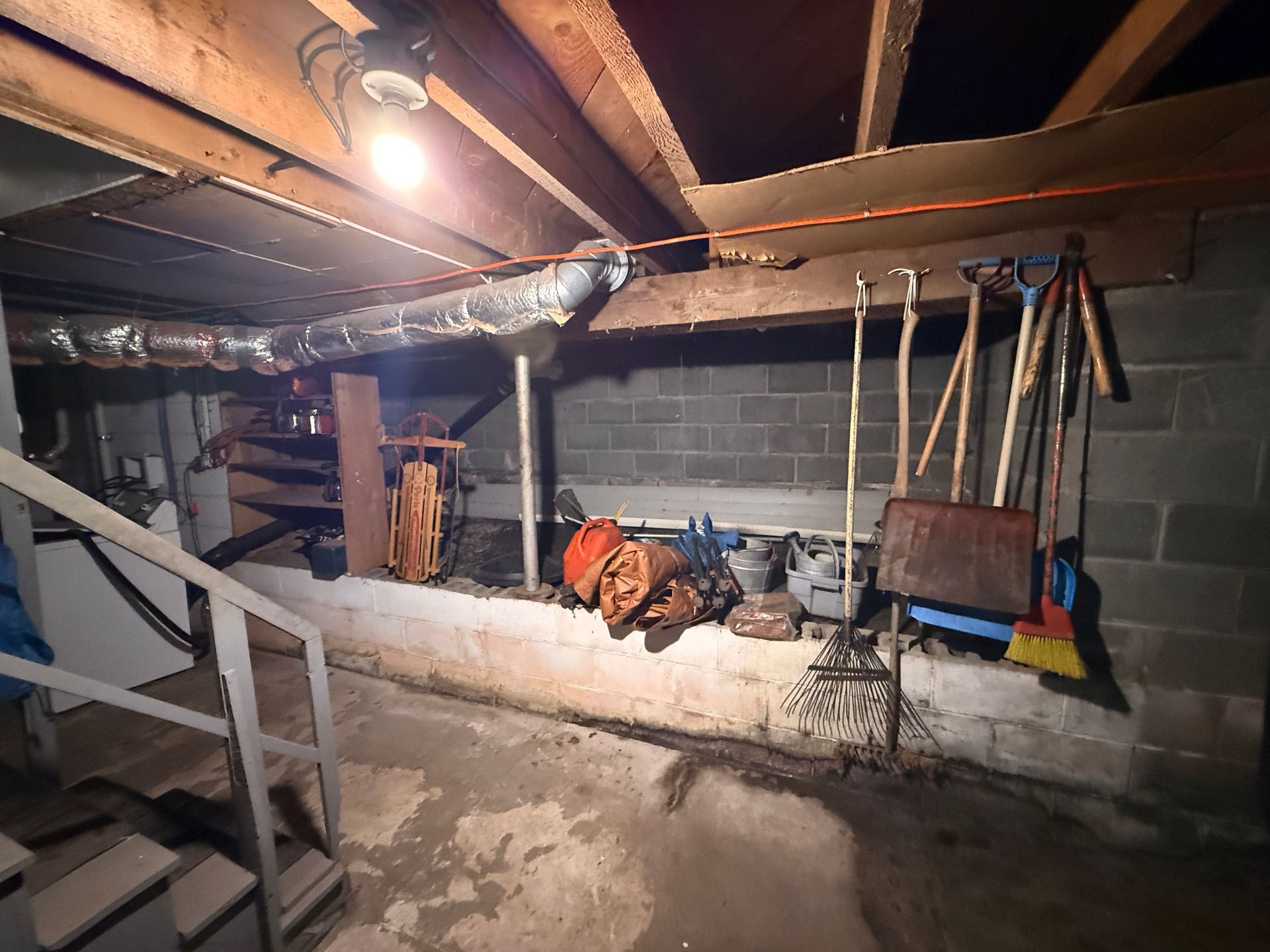 basement with exposed beams, cinderblock wall, and tools hanging above a concrete ledge.