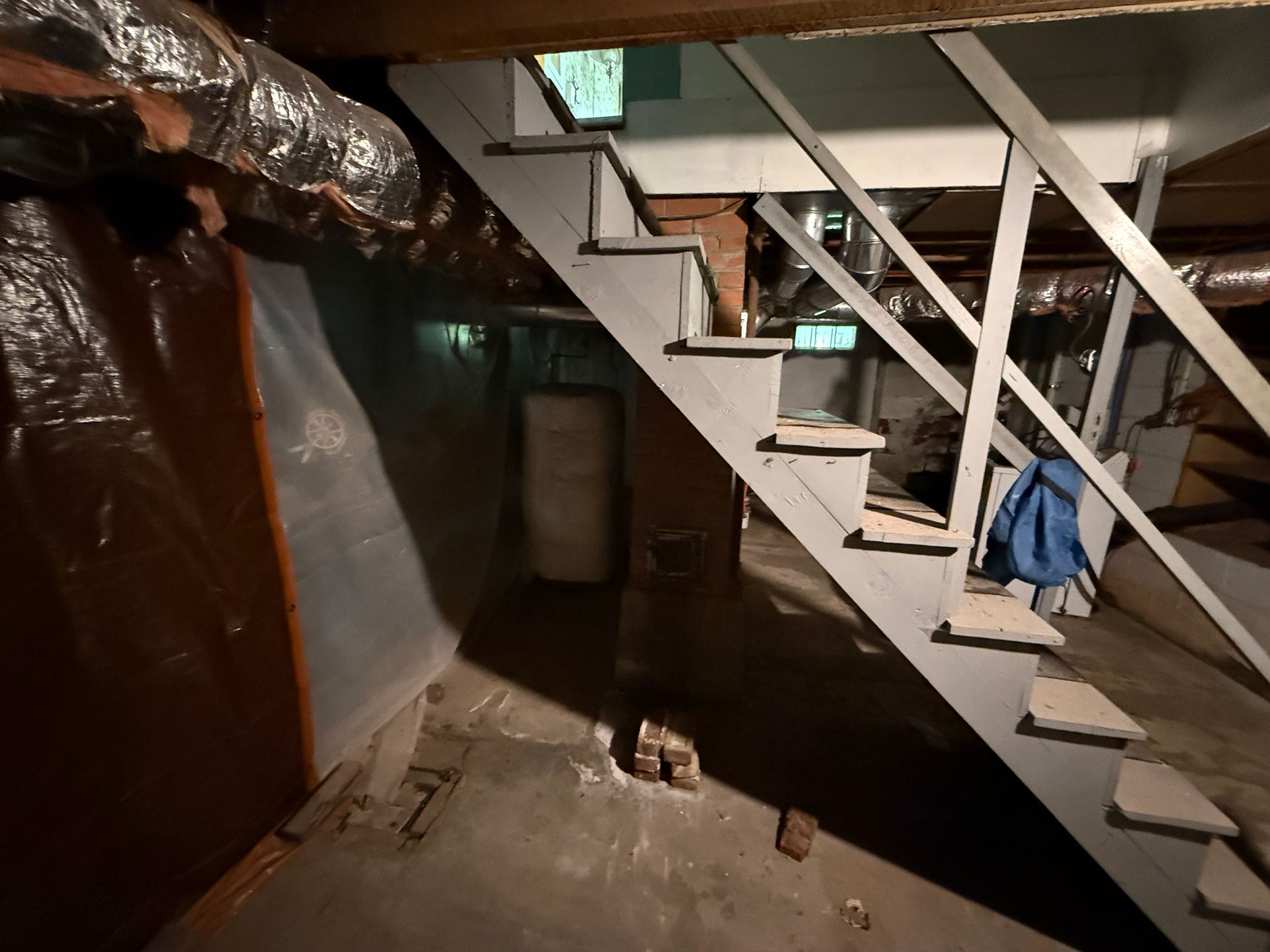 Basement crawlspace with a staircase, exposed pipes