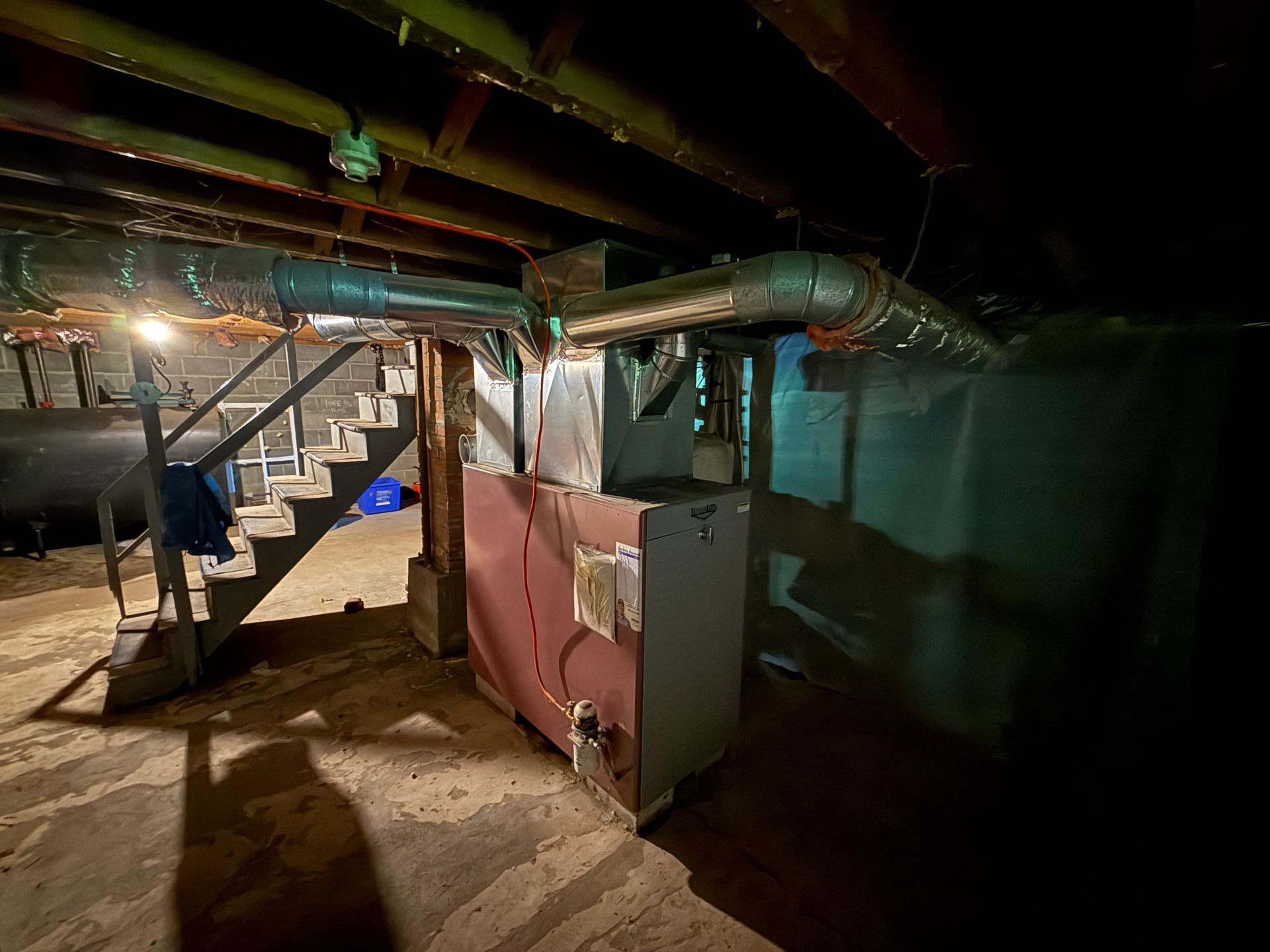 Basement with exposed beams, ductwork, and stairs beside a pink wall panel under dim lighting
