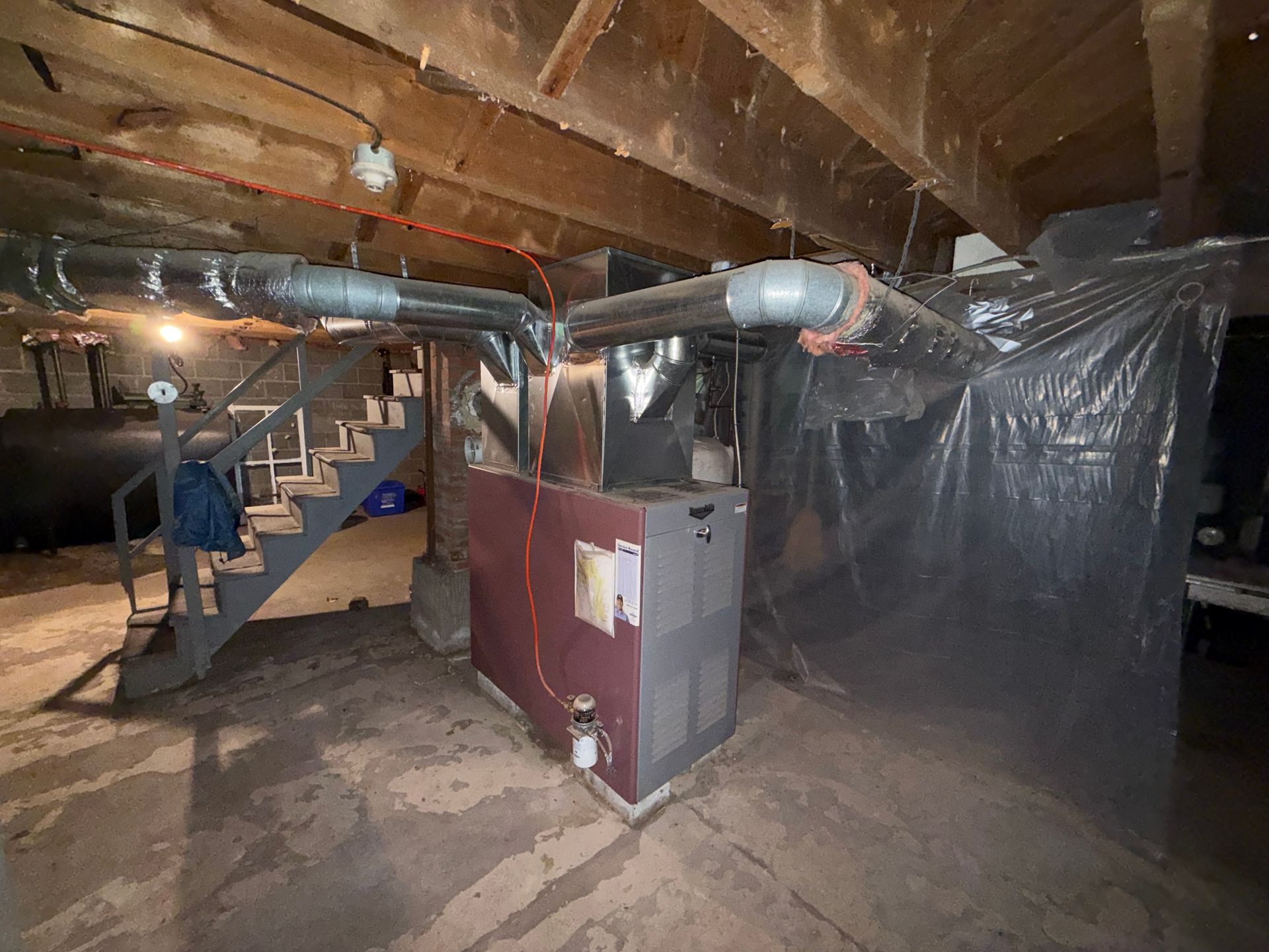 Basement utility area with furnace, exposed ductwork, stairs, and plastic sheeting on the right wall.