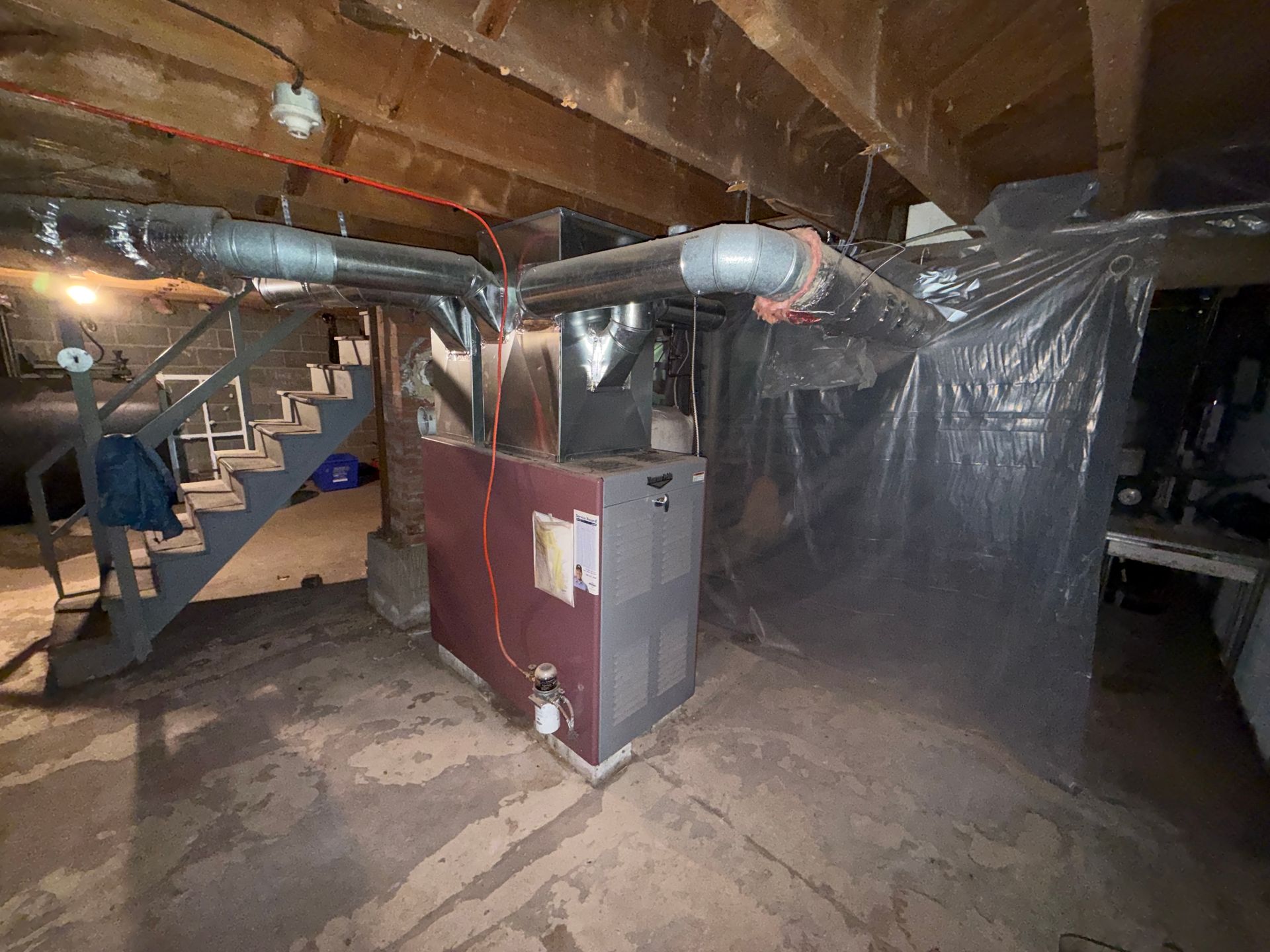 Basement utility area with furnace, exposed ducts, and plastic sheeting along the wall.