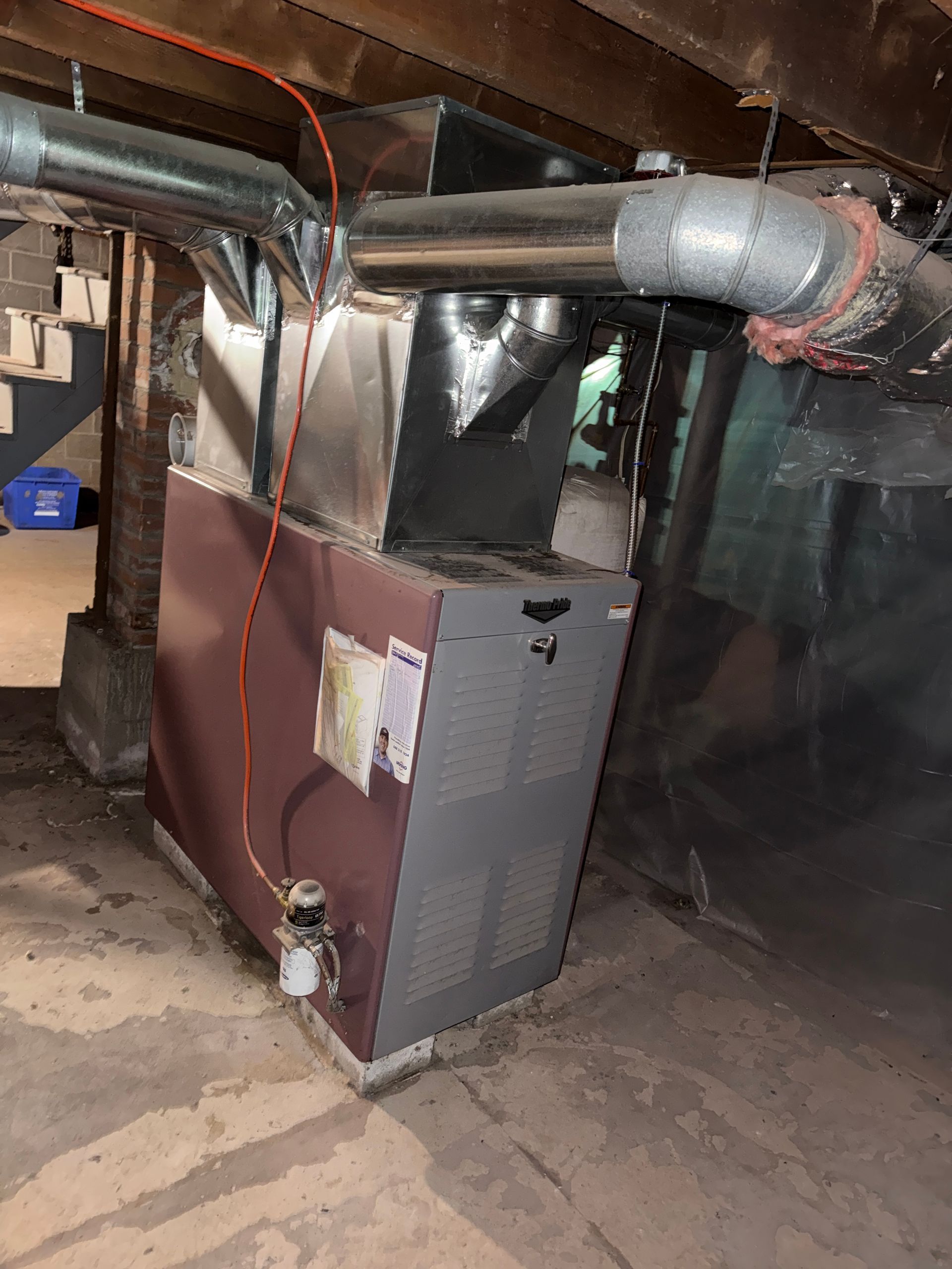 Furnace and ductwork in a basement, with insulation and exposed pipes.
