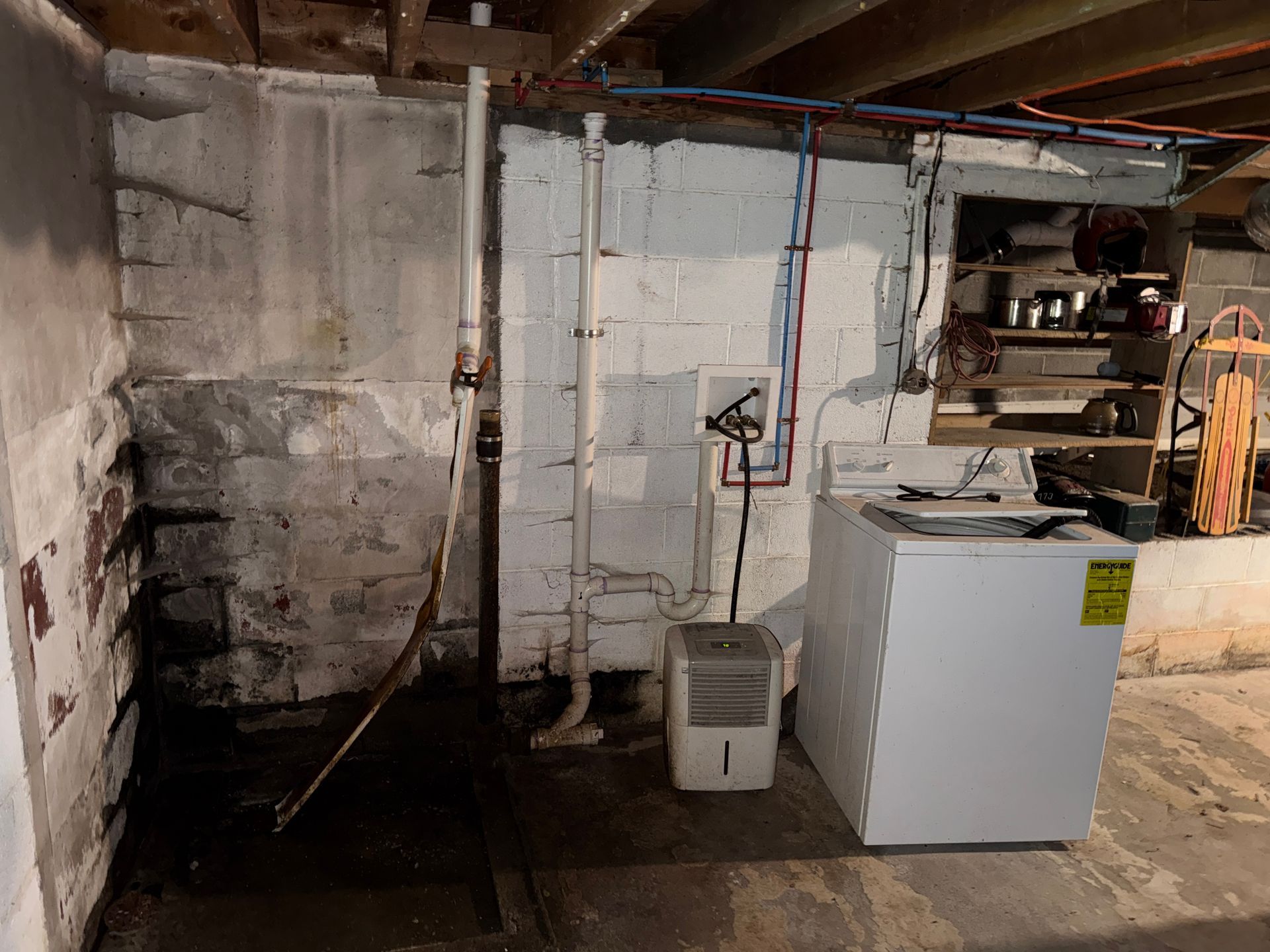 Basement utility area with a washer, pipes, utility sink, and exposed concrete walls.