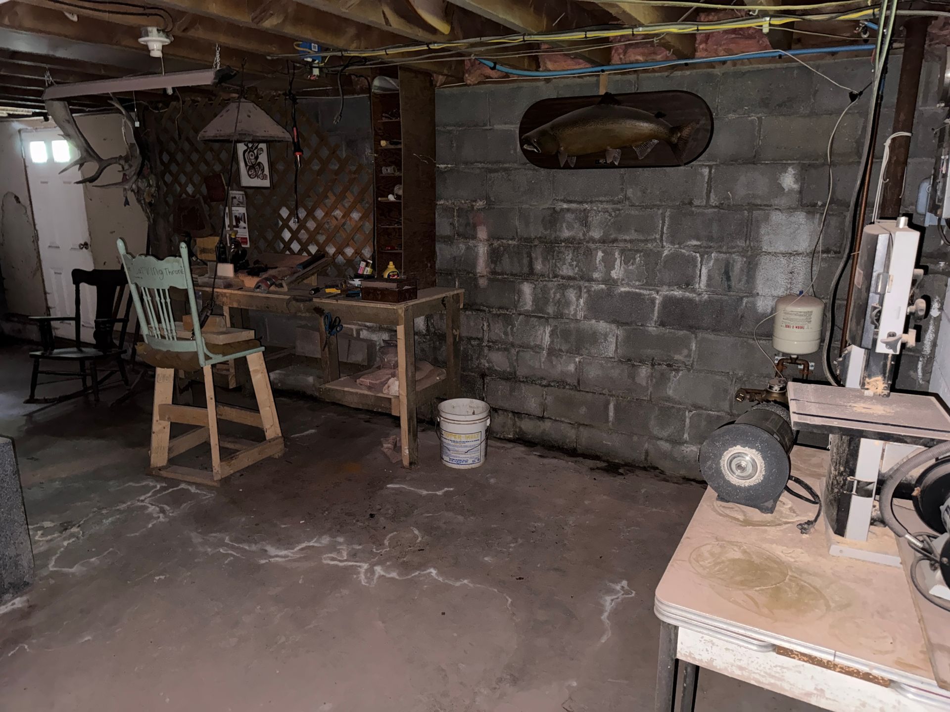 basement workshop with cinder block walls, workbench, chair, and tools under exposed ceiling beams