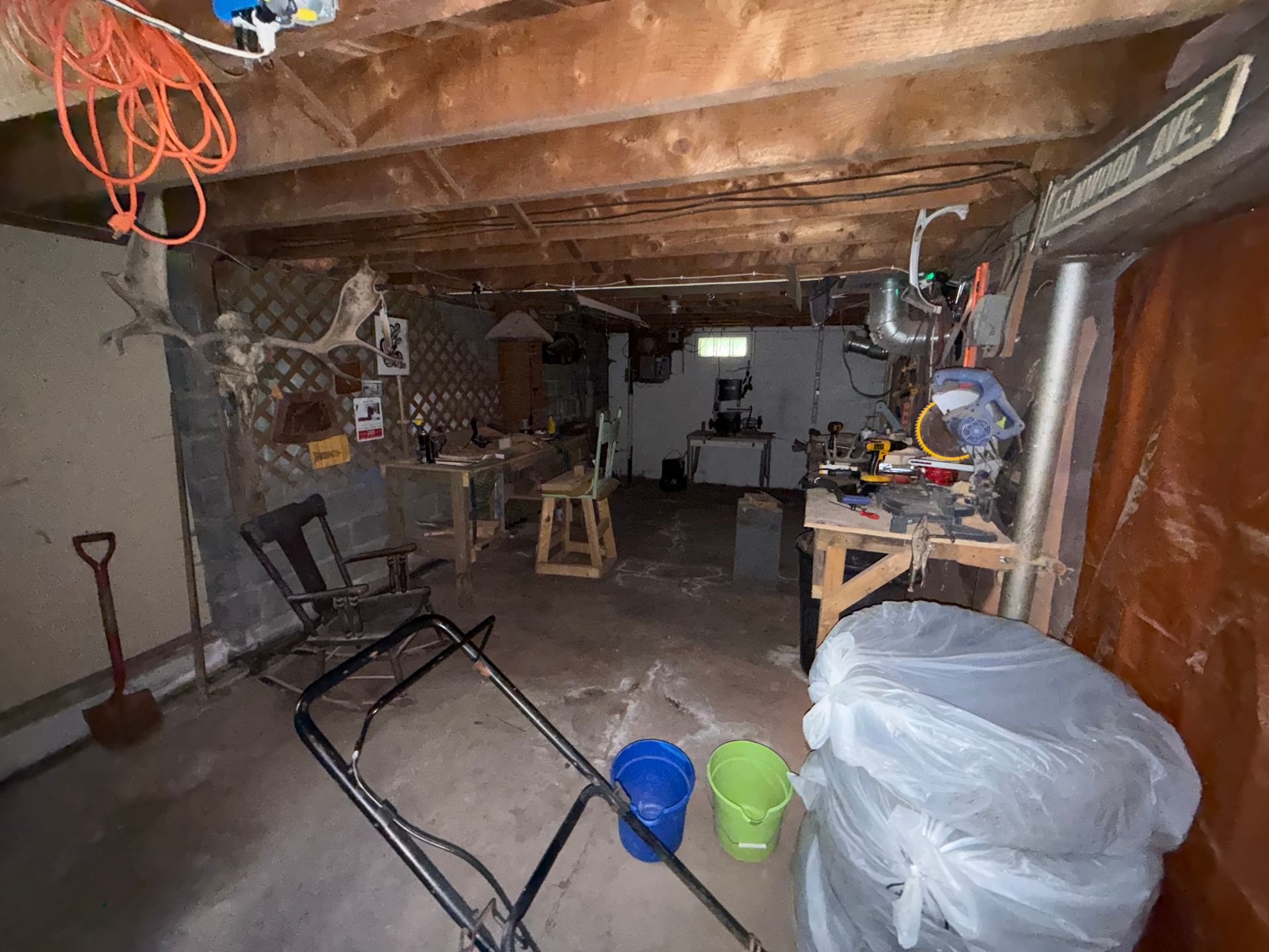 basement with exposed beams, tools, chairs, and buckets under lighting.