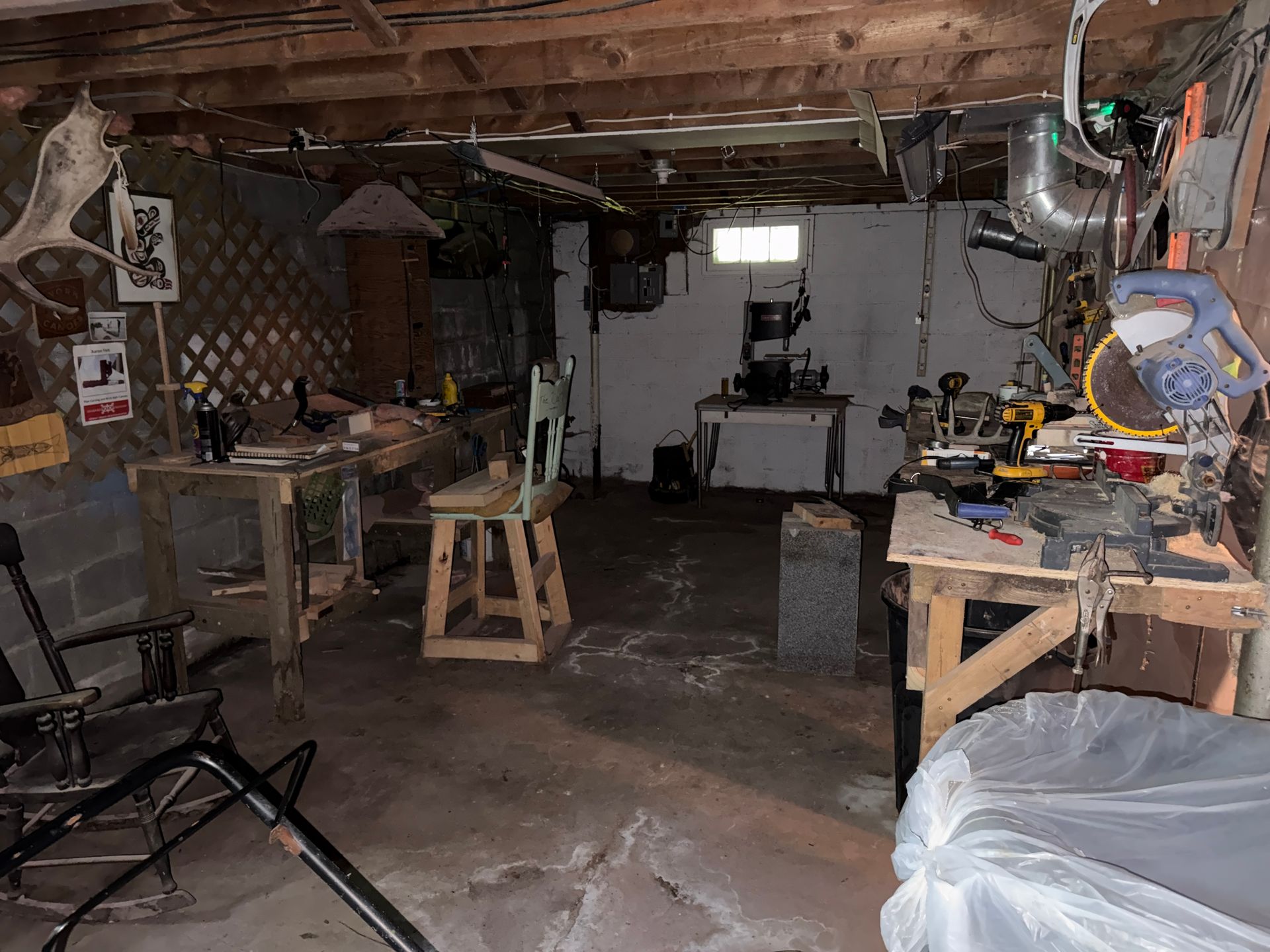 basement workshop with tools, benches, and a miter saw under exposed ceiling beams