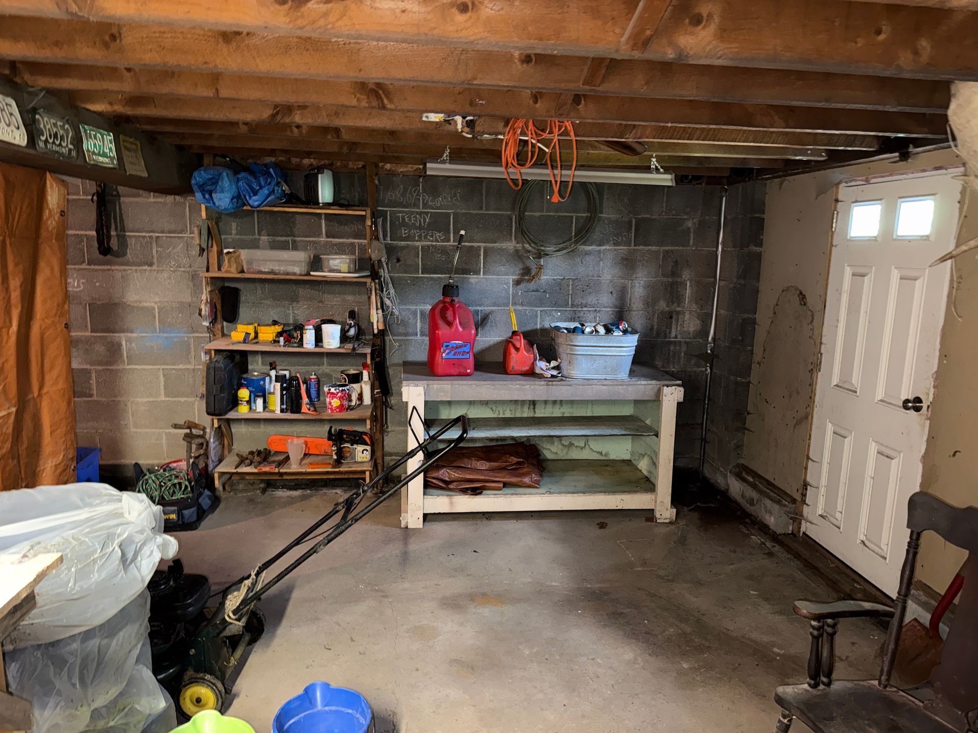 Basement workshop with shelves, tools, workbench, and a white door on the right.