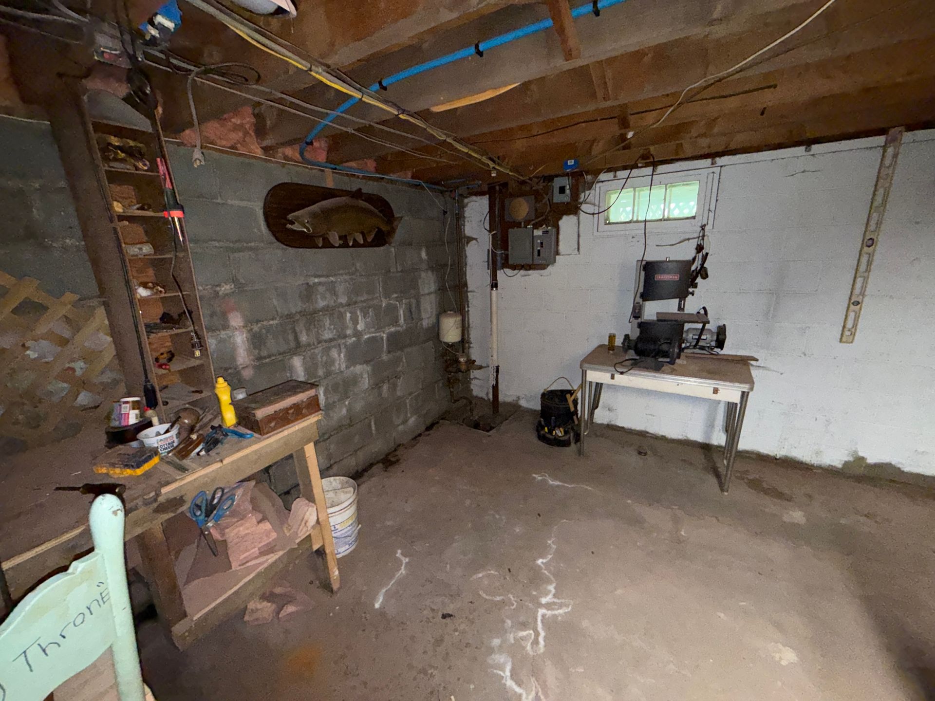 Small basement workshop with cinder block walls, workbench, ladder, and concrete floor.