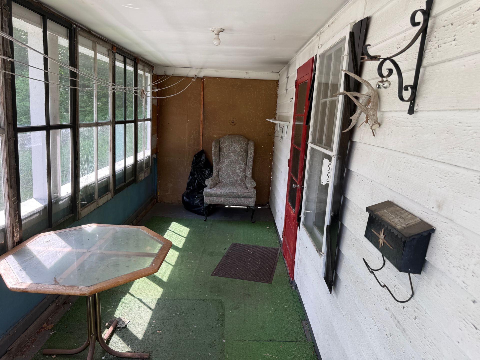 Covered porch with green carpet, octagonal table, rocking chair, and white siding along the wall.