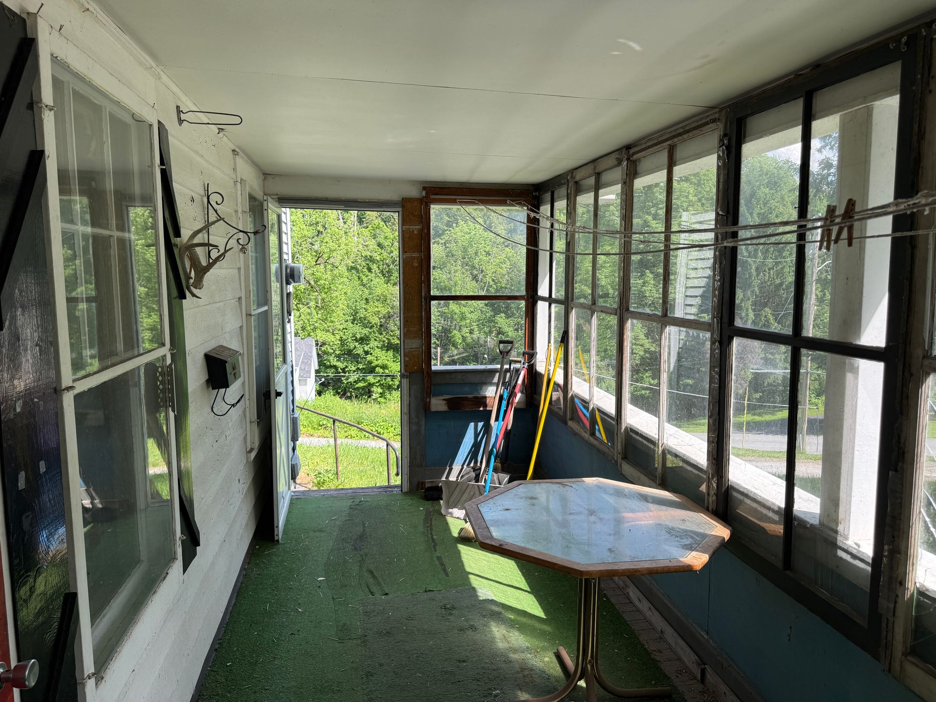 Sunlit screened porch with green carpet, windows, and a small table by the doorway