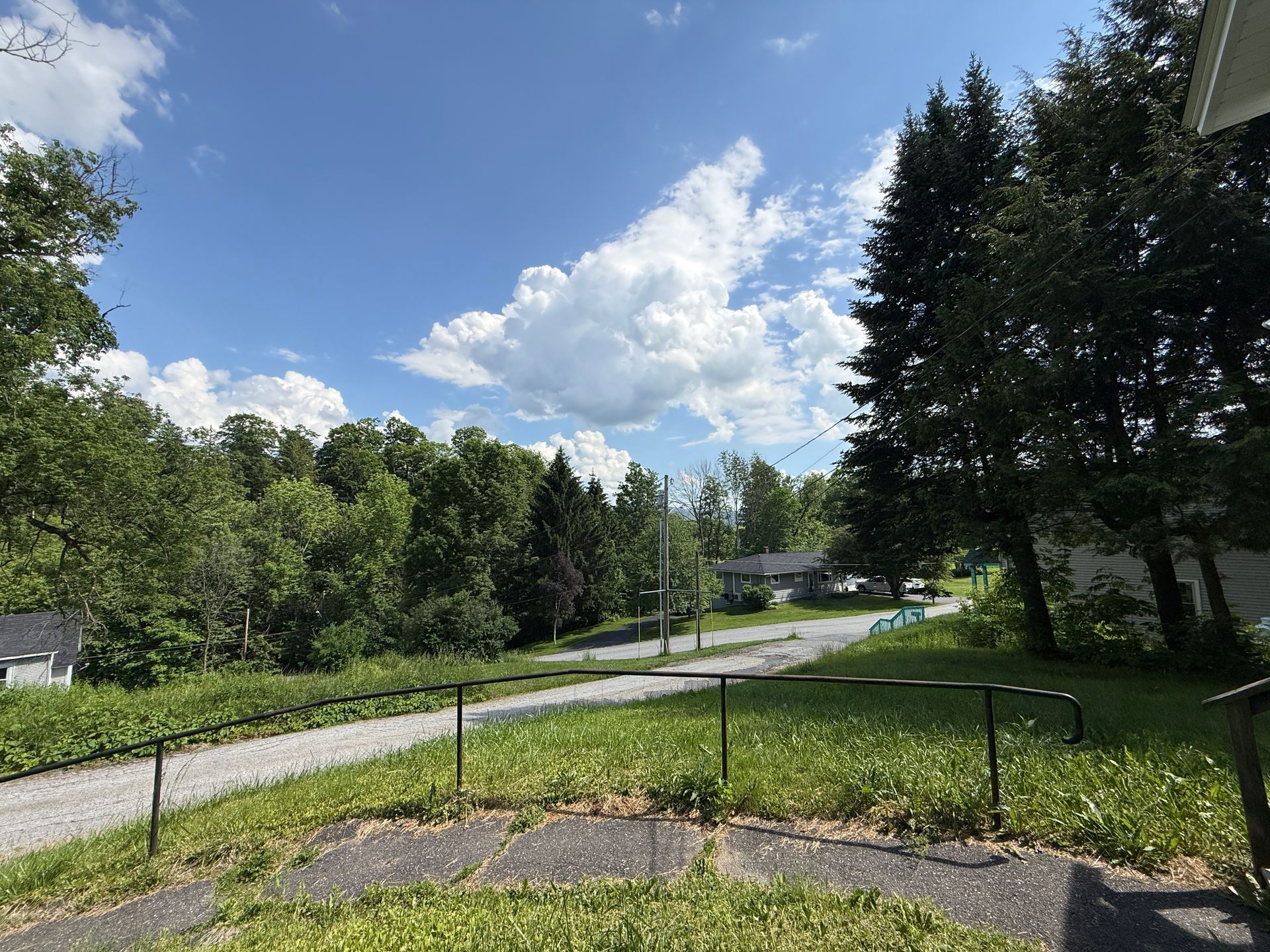 Gravel road curving through a green rural neighborhood under a blue sky with fluffy clouds