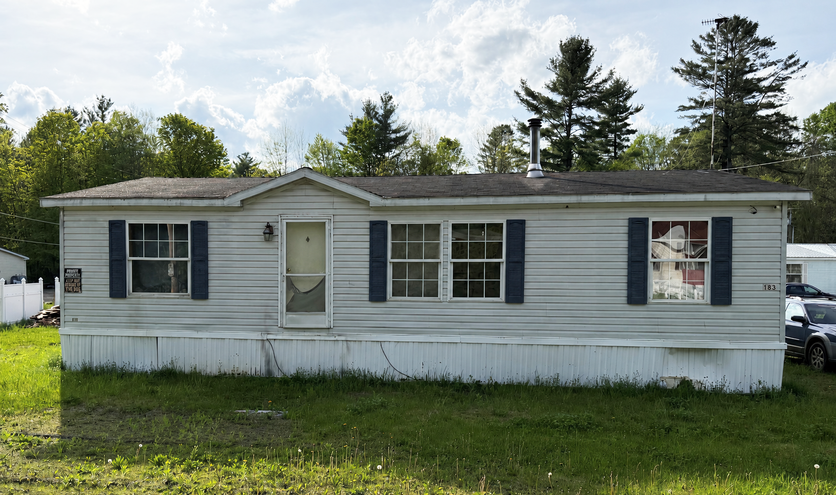 Small white mobile home with blue shutters in a grassy yard on a sunny day