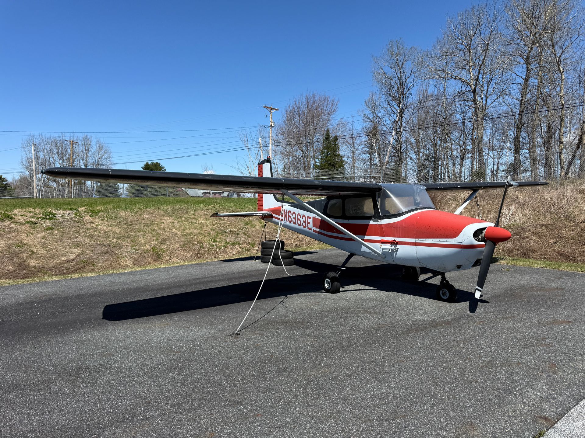 Red-and-white small airplane parked on a paved surface under a clear blue sky