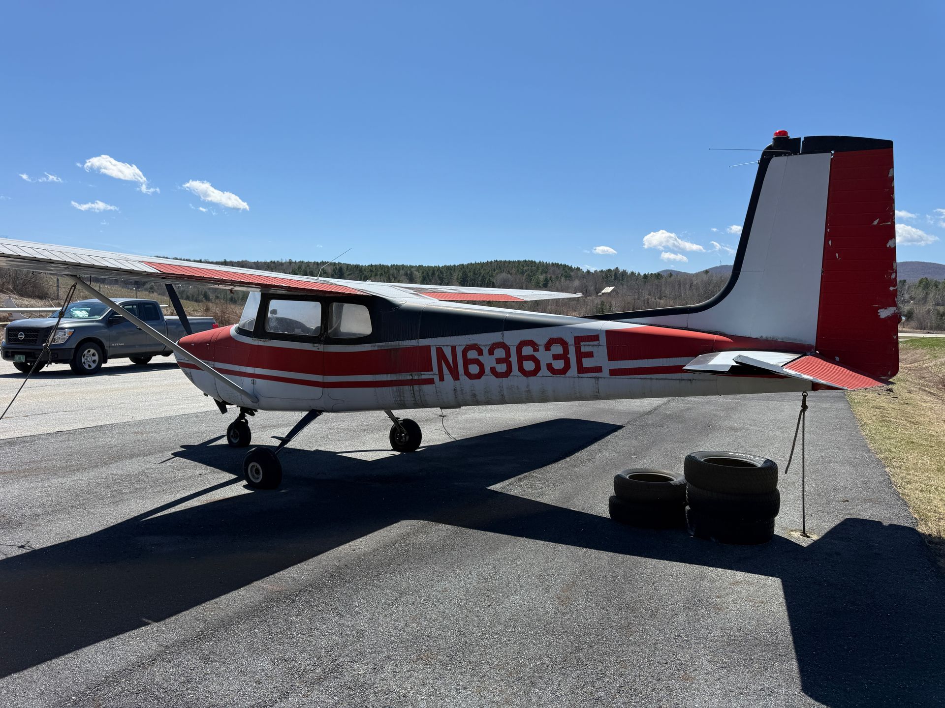 Small red-and-white single-engine airplane parked on a sunny tarmac with mountains in the background