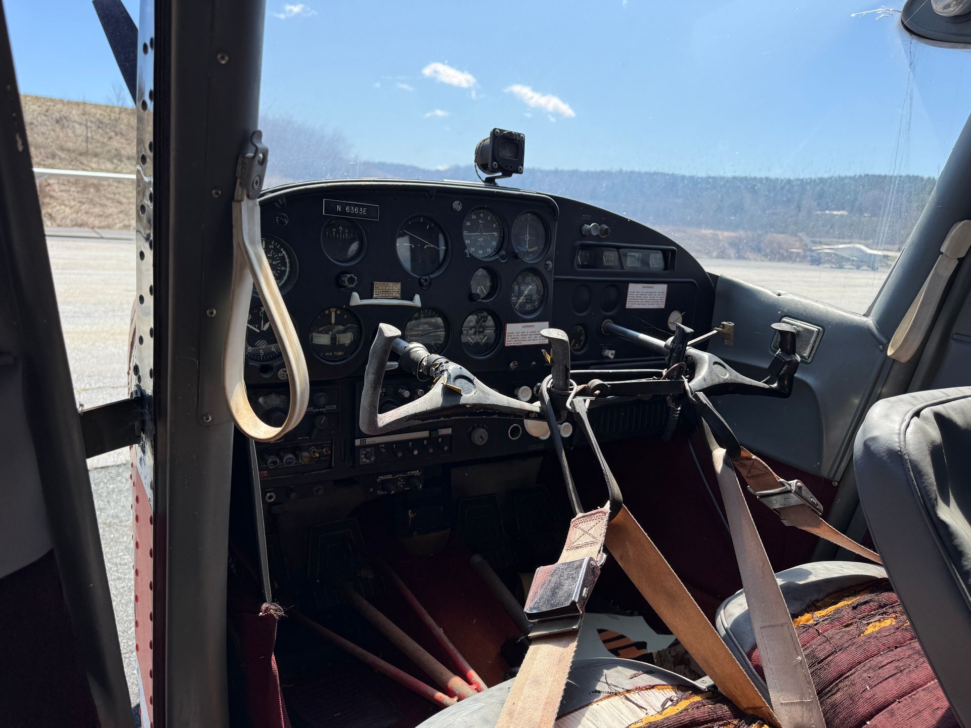 Small airplane cockpit with controls, seat belts, and mountains visible through the windshield.