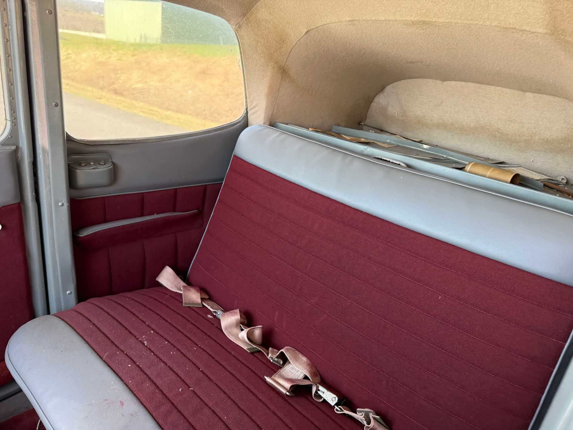 Airplane interior with red and gray bench seat and a beige headrest by the window
