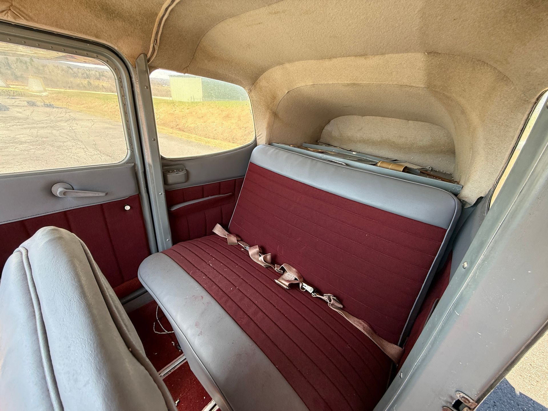 Vintage airplane interior with burgundy bench seats and beige trim, seen from the back seat