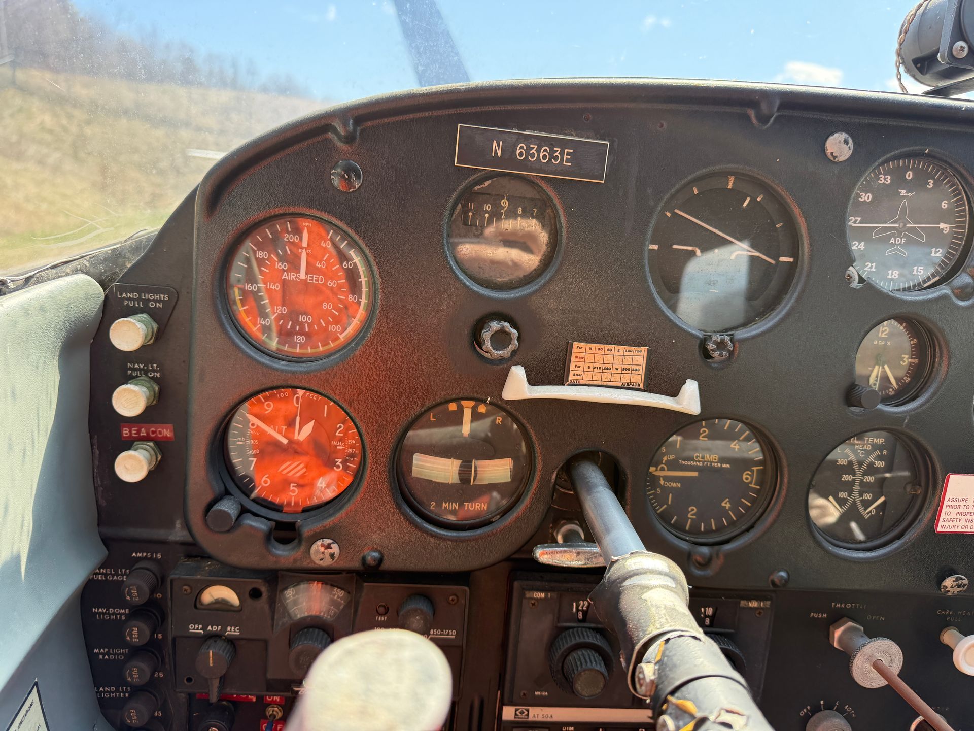 Cockpit dashboard with orange-lit gauges, control stick, and analog flight instruments against a bright sky.
