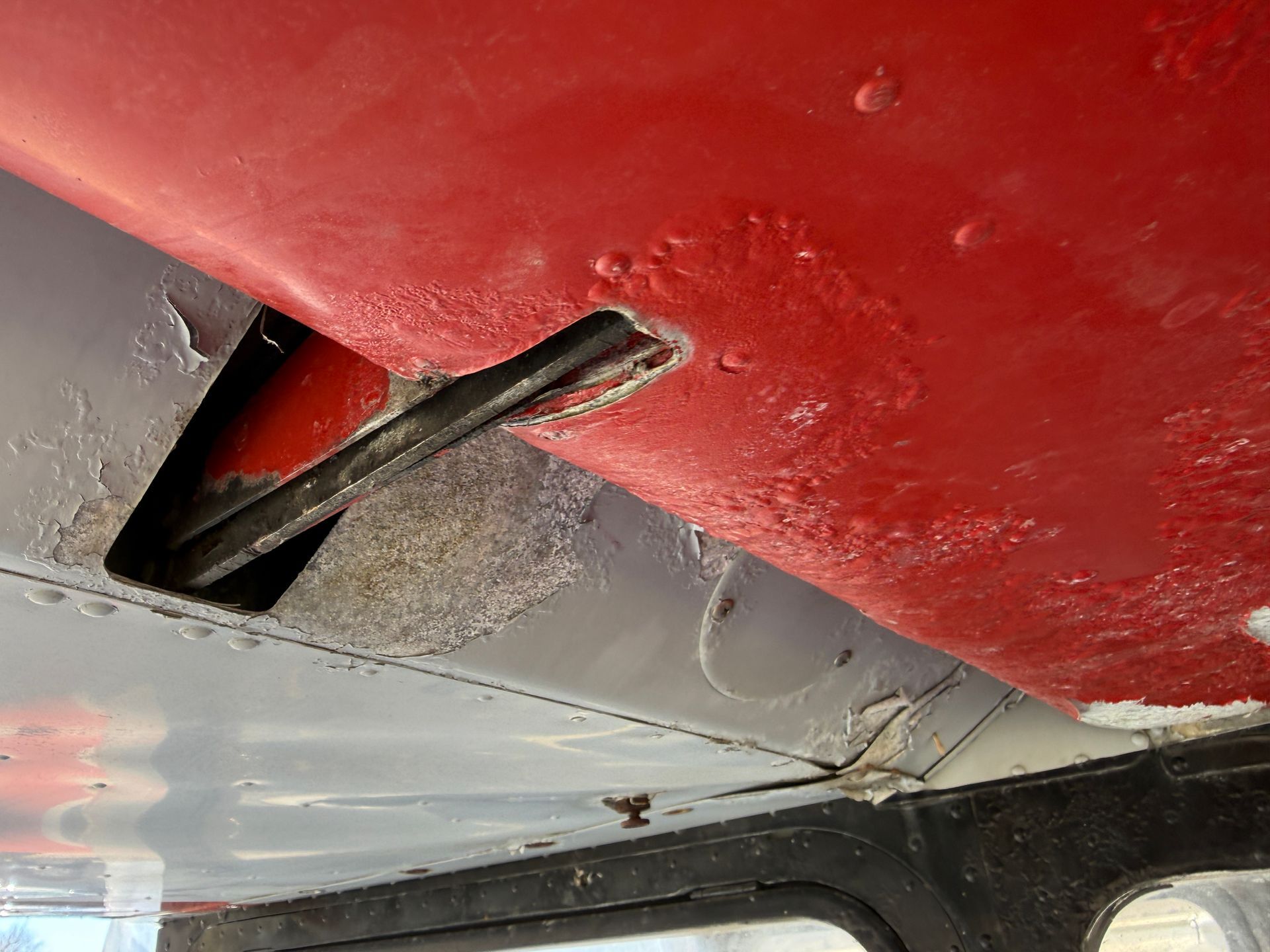 Close-up of a red airplane underside with a metal lever protruding through a panel opening.