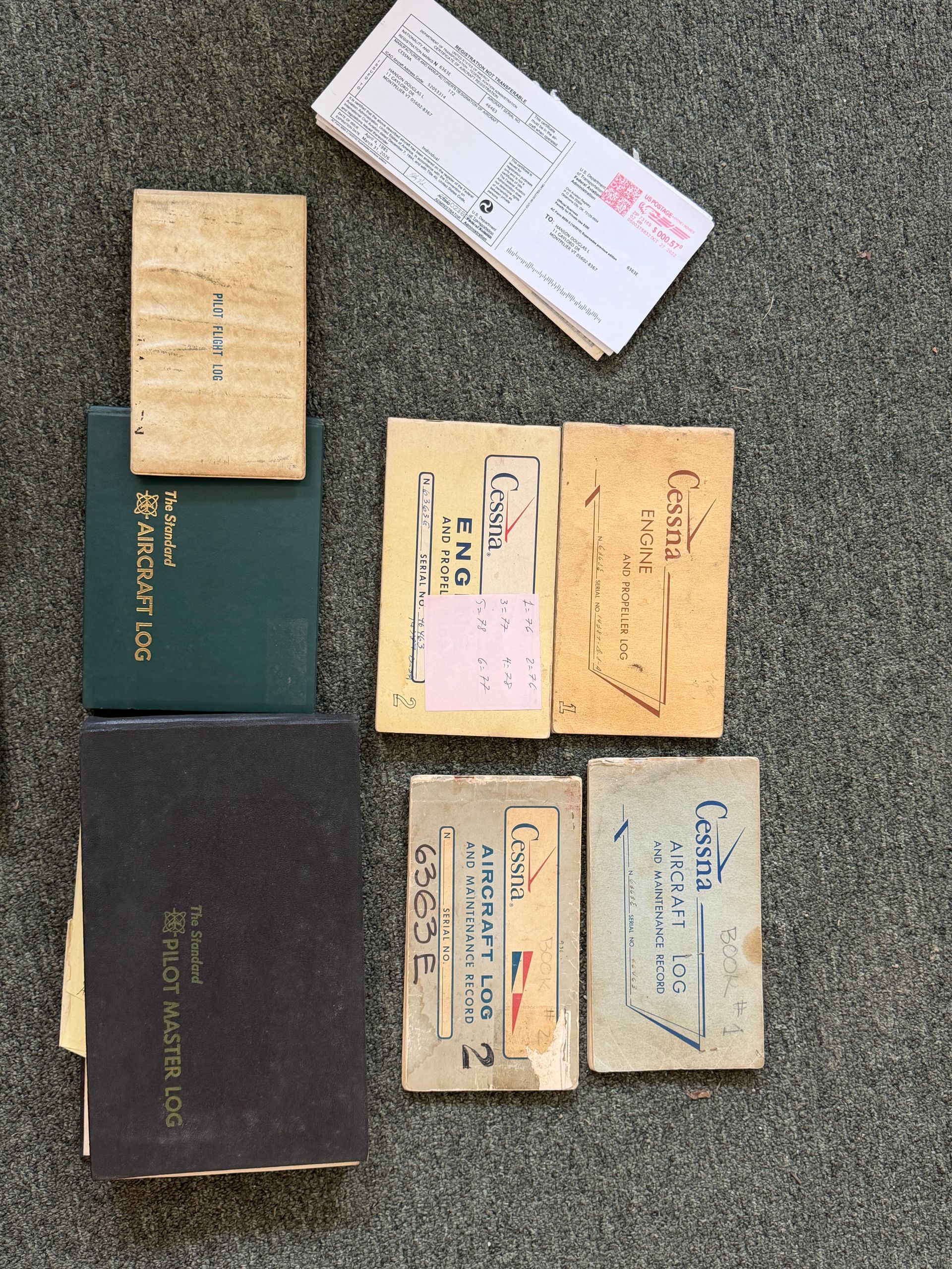 Assorted paper envelopes and booklets in tan, green, white, and black arranged on a textured gray surface