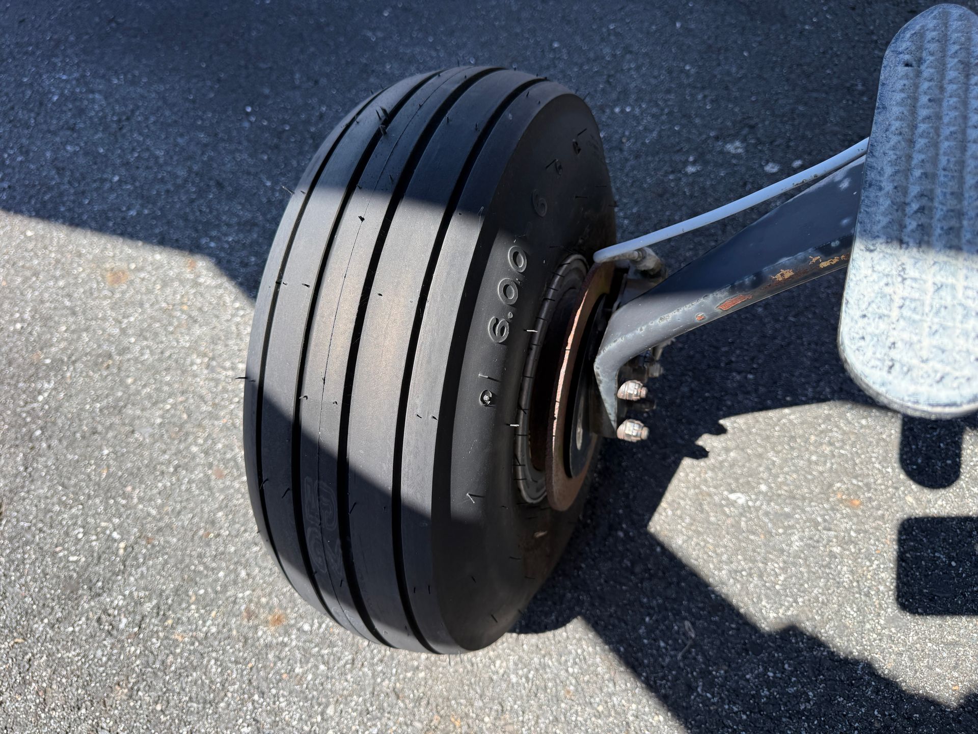 Close-up of a small aircraft wheel on a runway, with a metal strut and shadow on pavement.