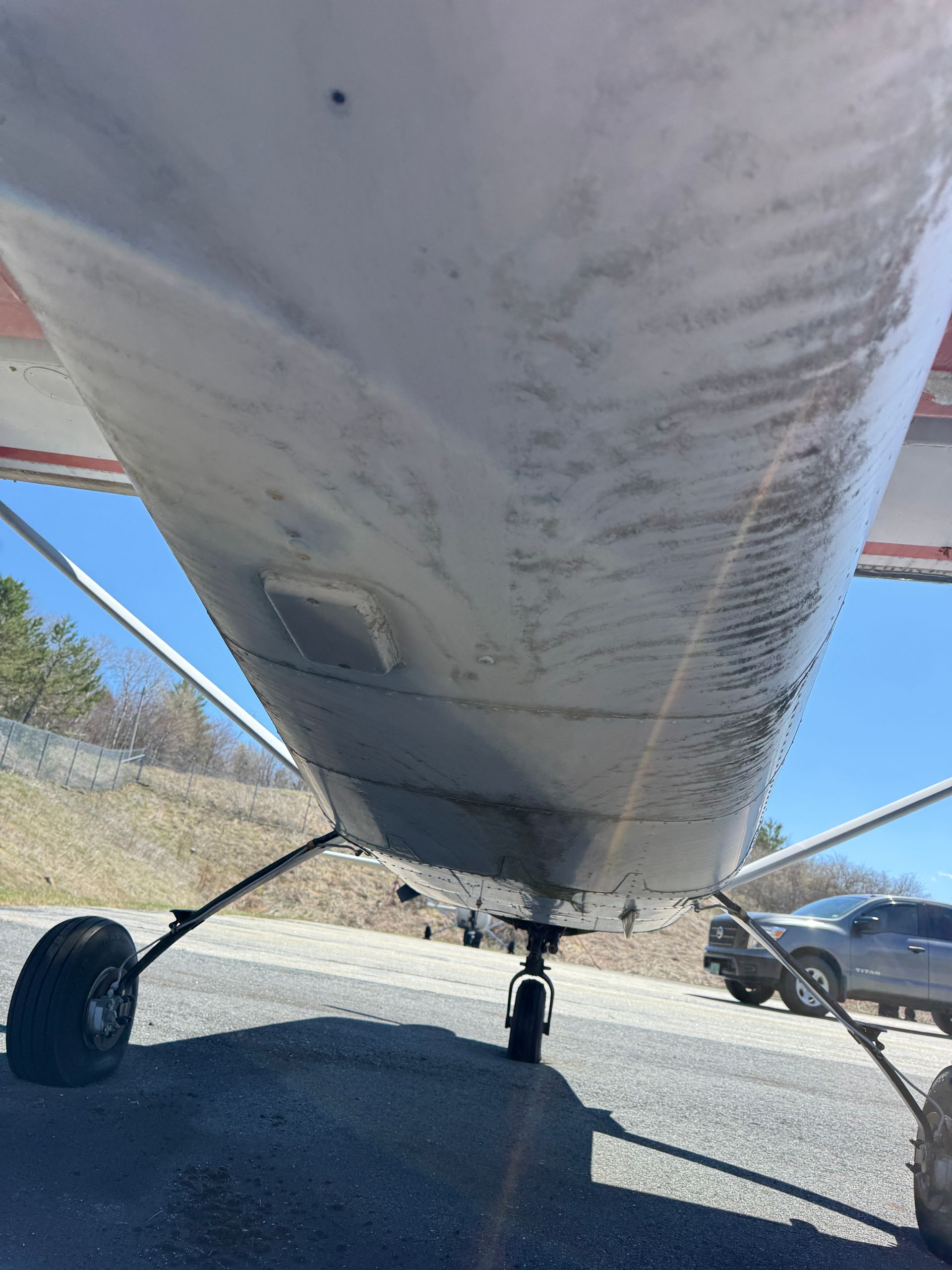 Underside of a small airplane on landing gear, parked on gravel