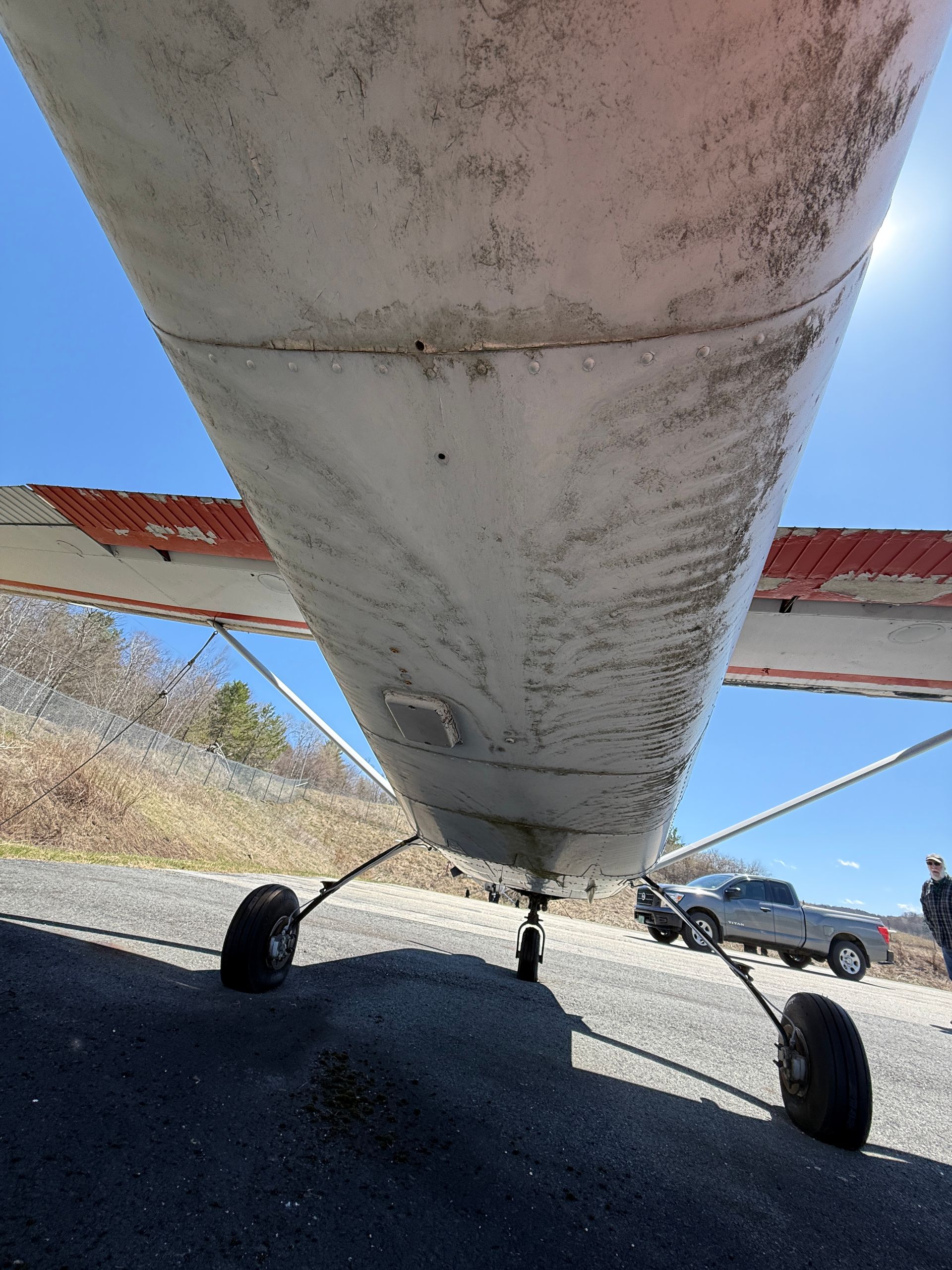 Underbelly view of a small airplane on a runway, showing landing gear, wings.