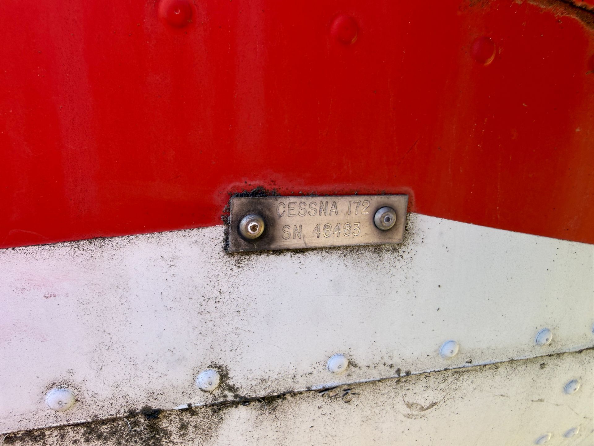 Close-up of a red-and-white plane hull with a small metal nameplate.
