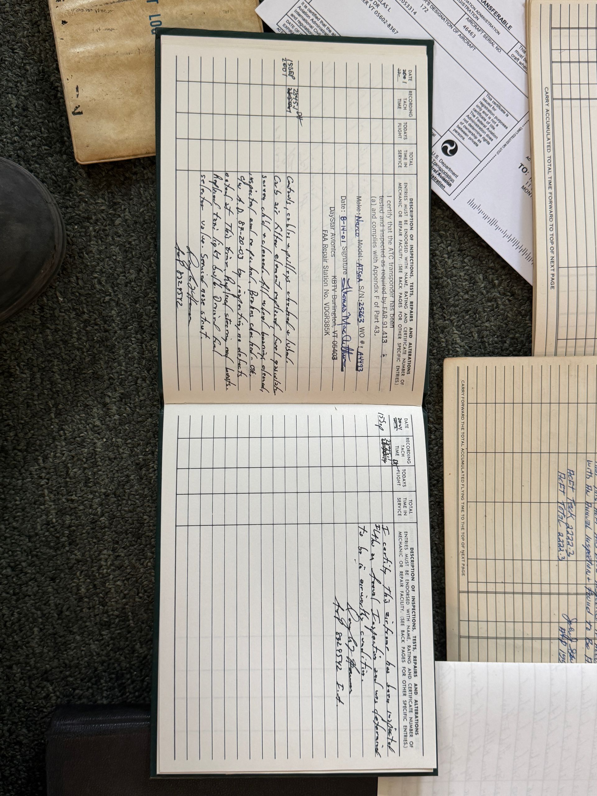 Two handwritten forms and one blank form laid on a dark carpet beside a wooden surface.