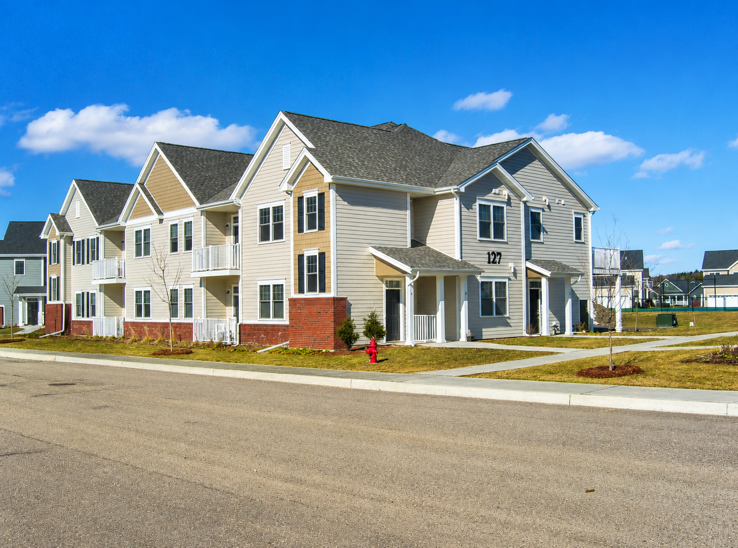 White two-story townhouse with gray roof, front porch, small lawn, and sidewalk in a suburban neighborhood