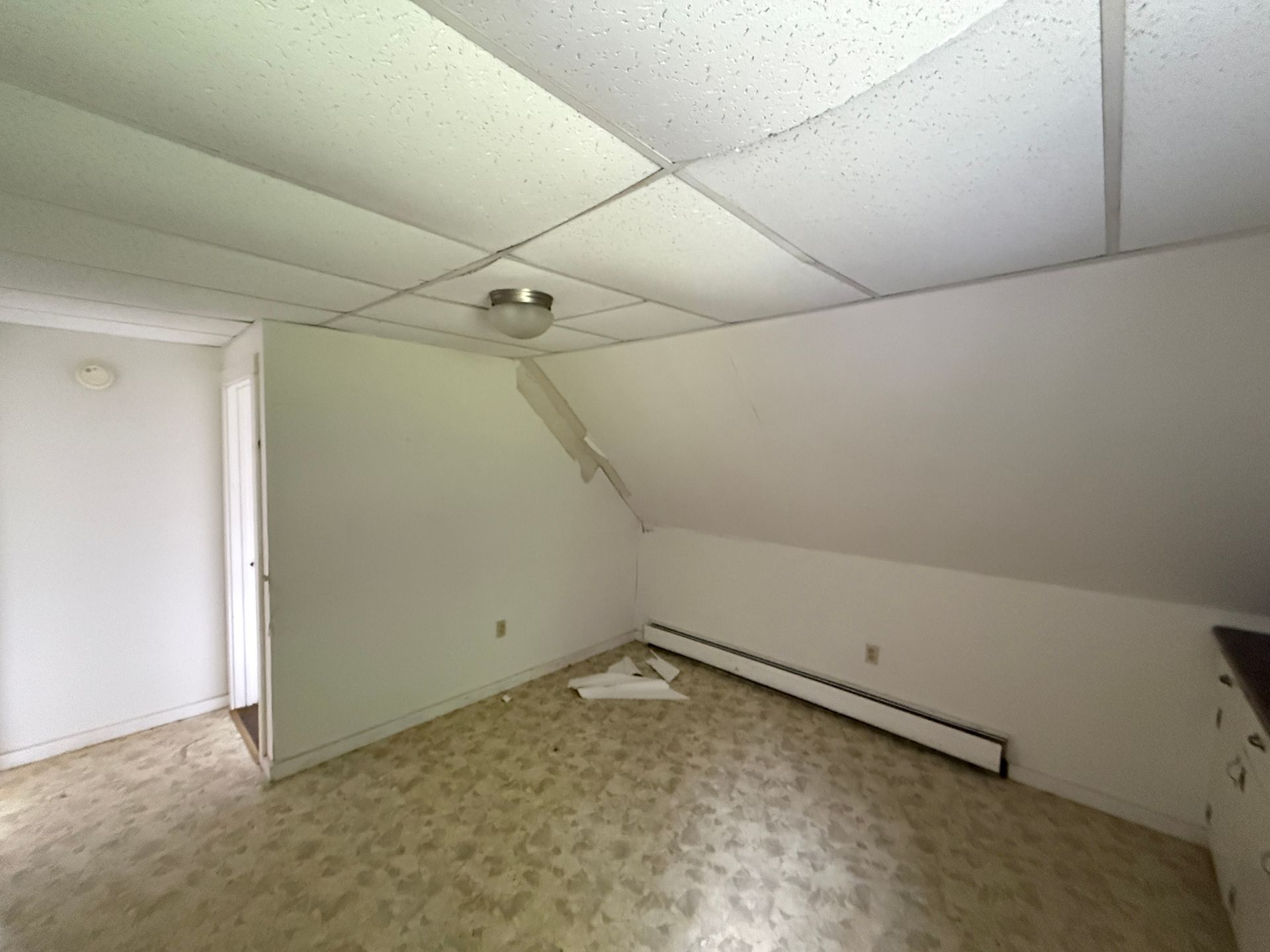 Small empty attic room with sloped ceiling, patterned carpet, and a ceiling light.