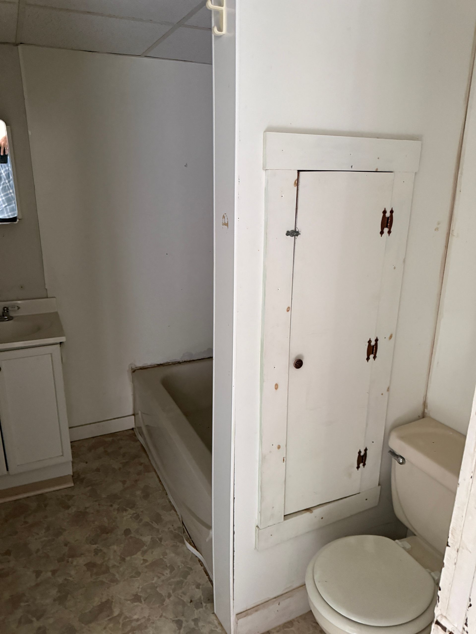 Small bathroom with toilet, bathtub, and white access panel on the wall.