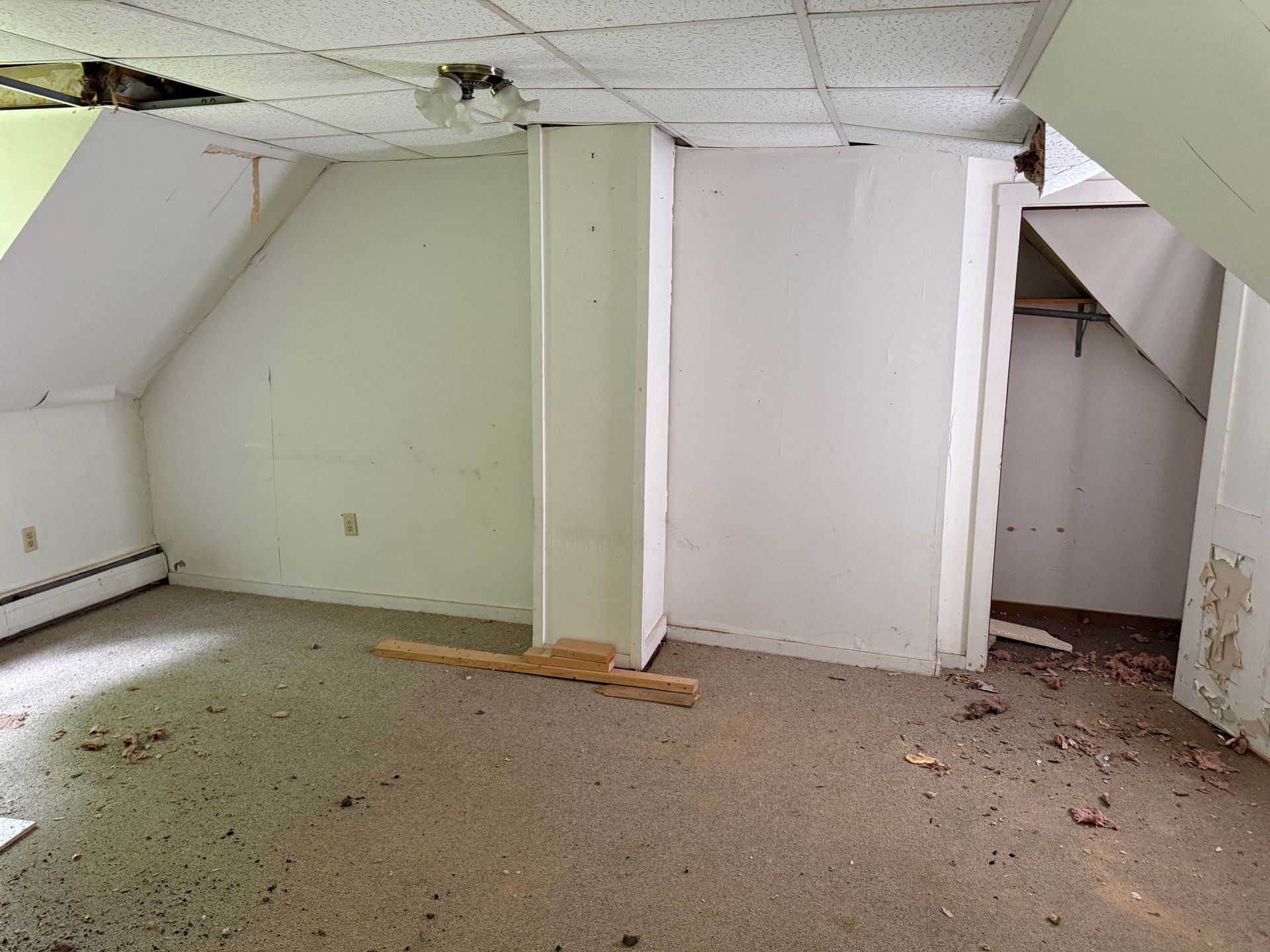 Empty attic room with slanted ceiling, white walls, exposed beams
