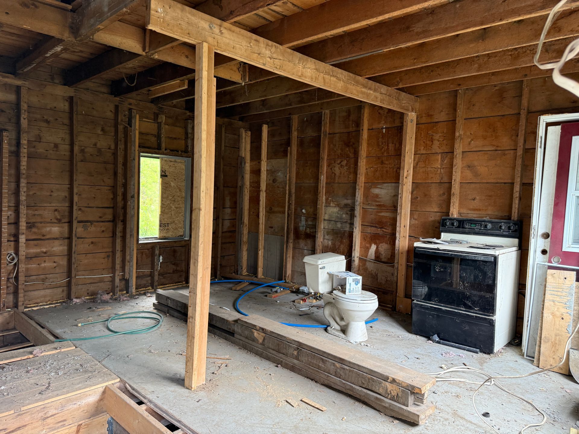 Interior of a stripped room under renovation, with exposed studs, a toilet, stove