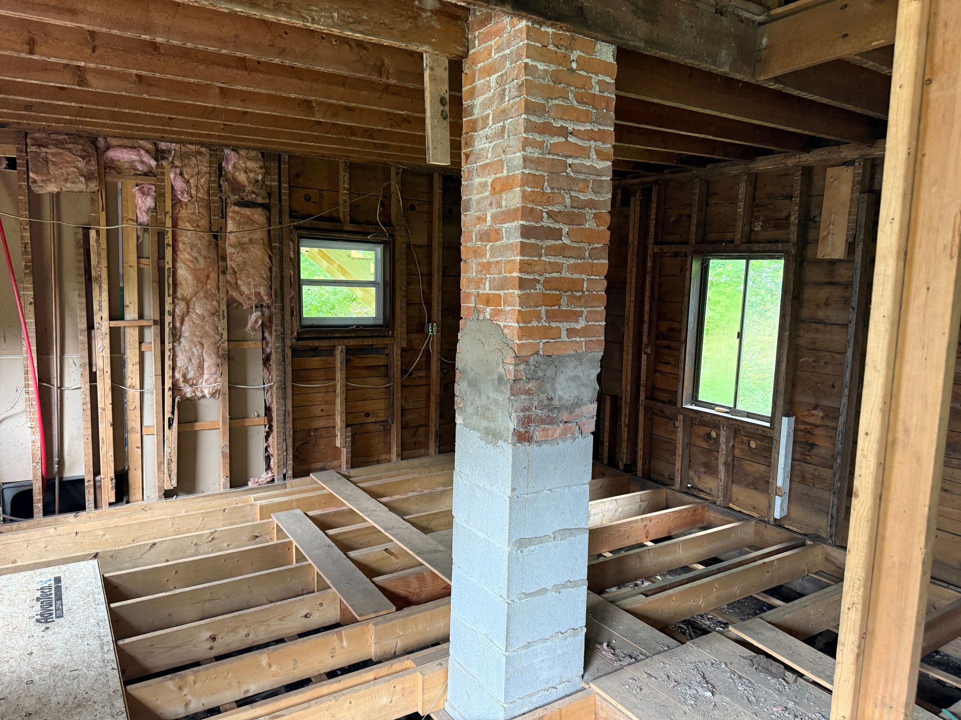Exposed interior of a house under renovation, with wood framing, brick chimney, and open floor joists.