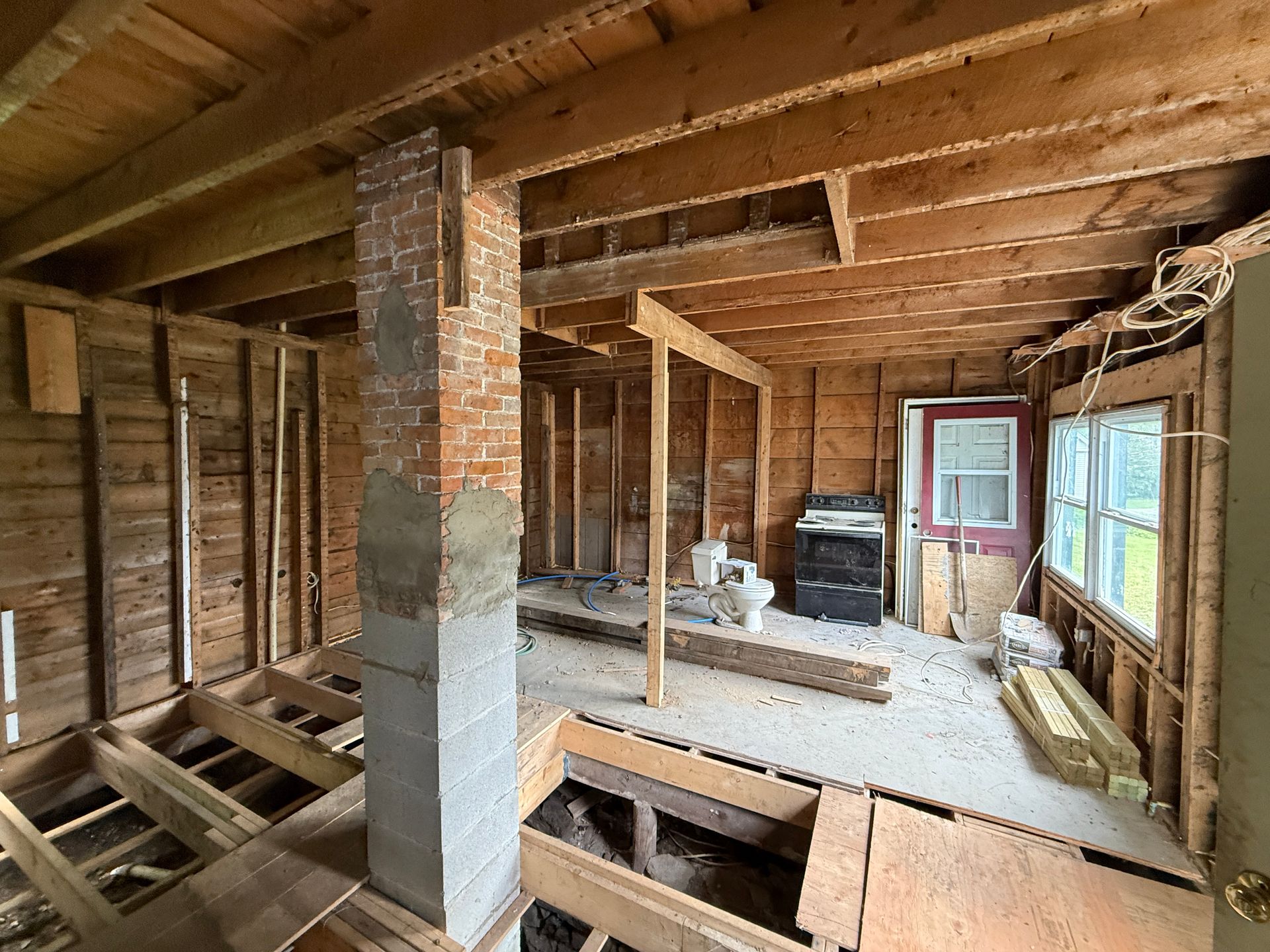 Interior of a house under renovation with exposed studs, beams, and a partially open floor.