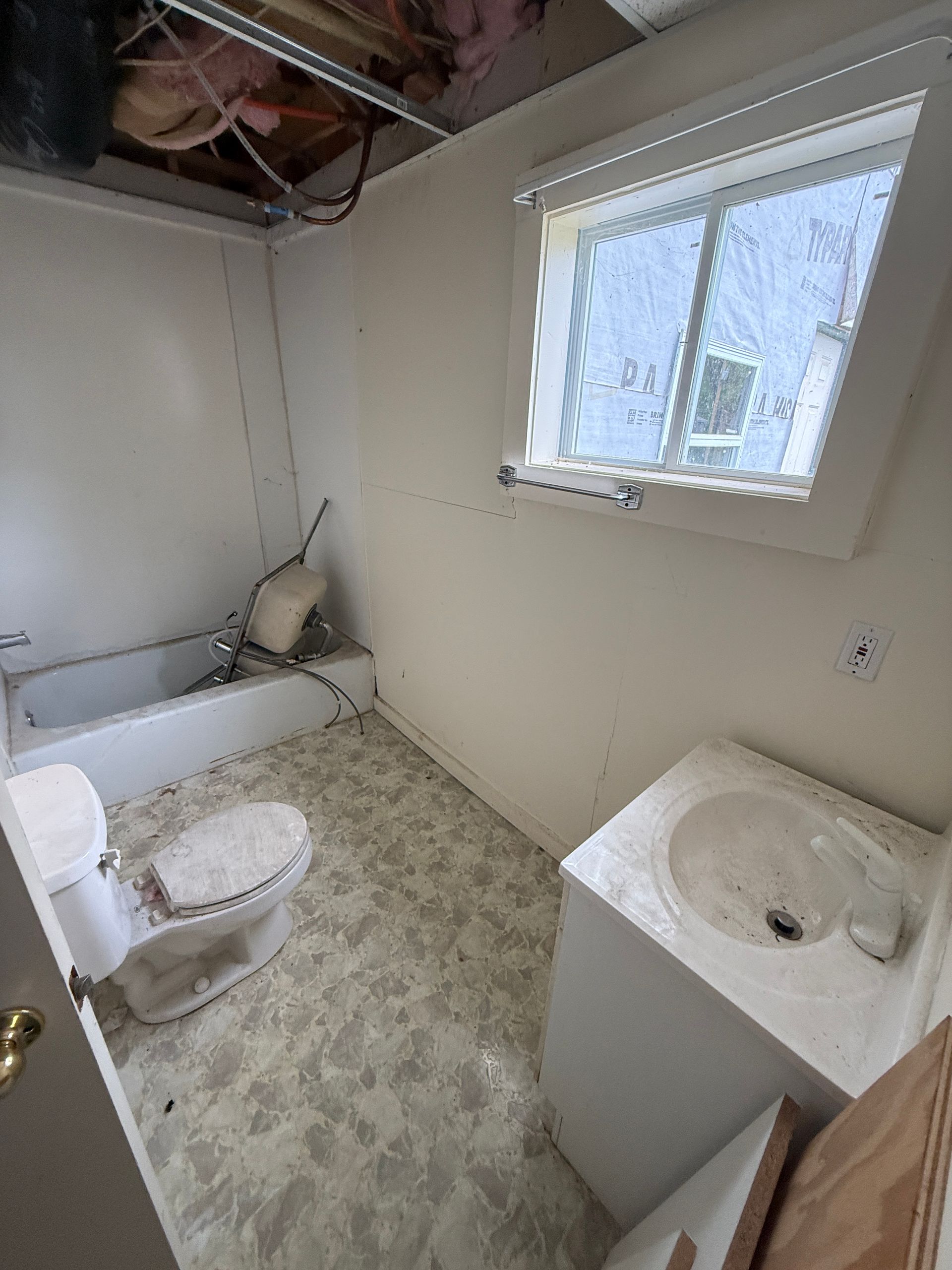 Small bathroom with toilet, bathtub, and sink under a window