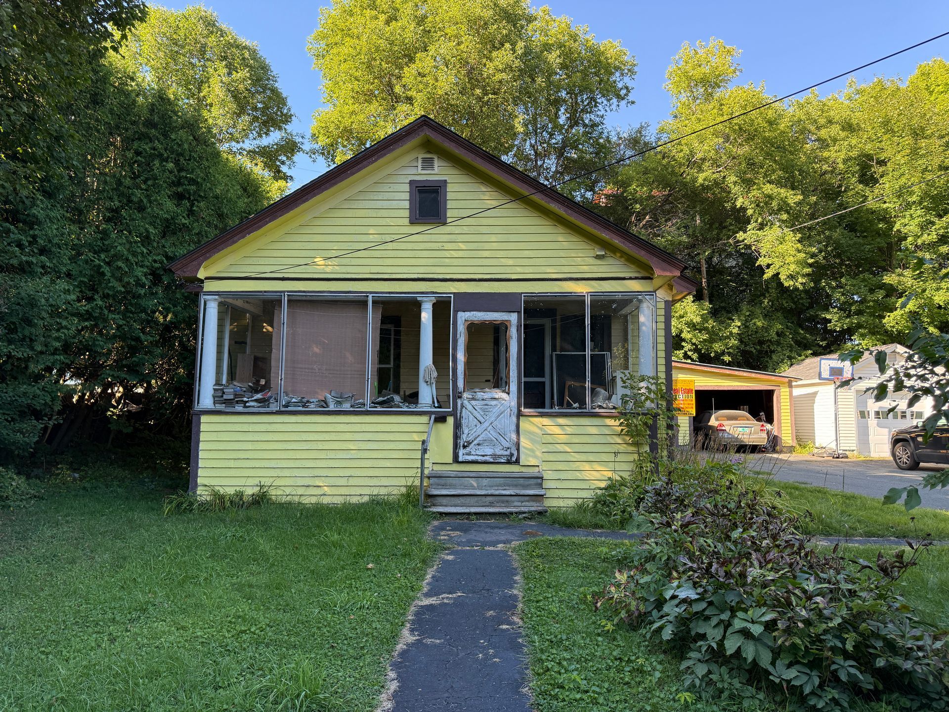 Yellow house with a front porch, centered walkway, and trees in the yard