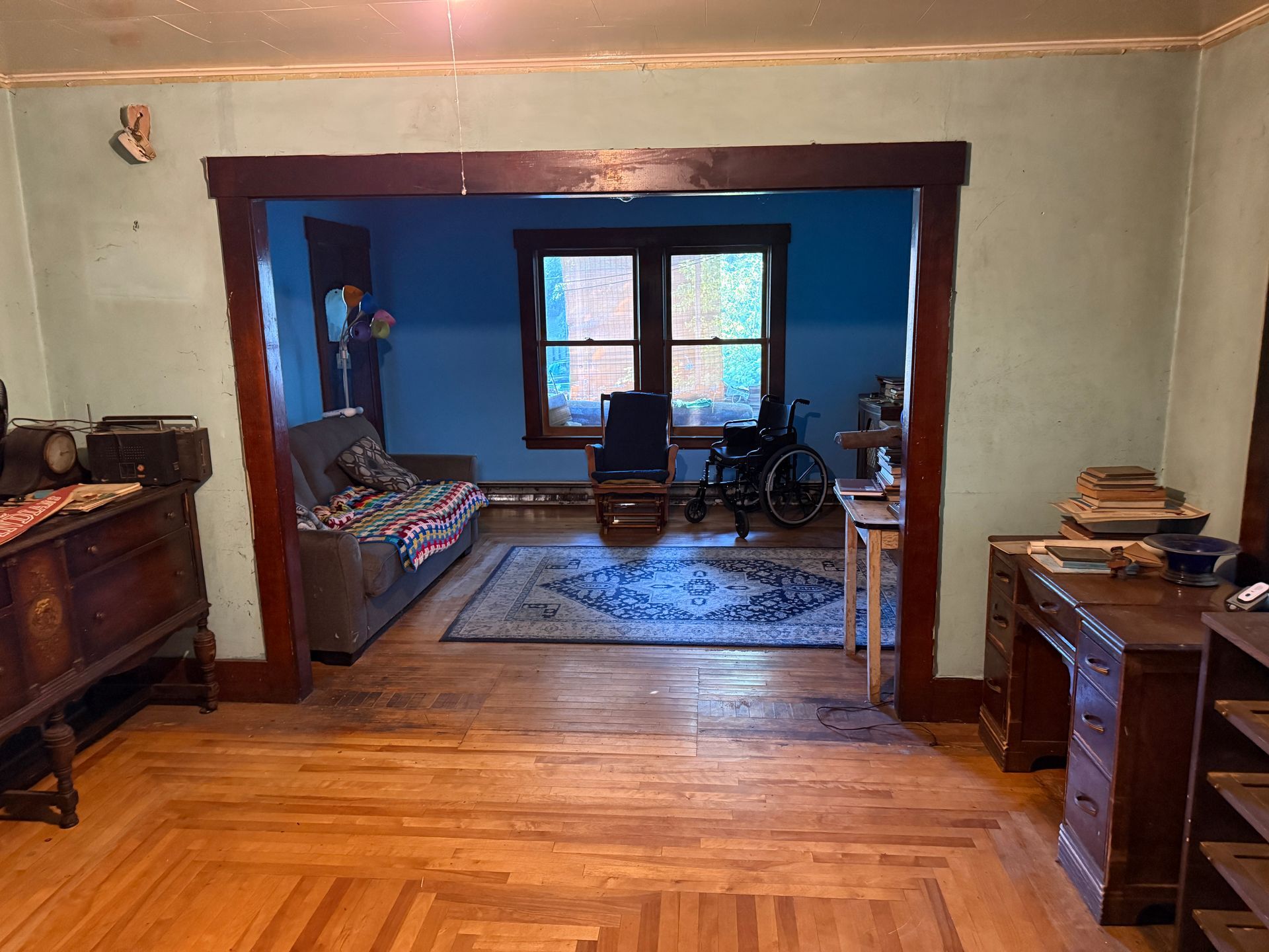 Wood-floored room with dark wood trim, doorway to a blue sitting room, chairs, rug, and desks on both sides