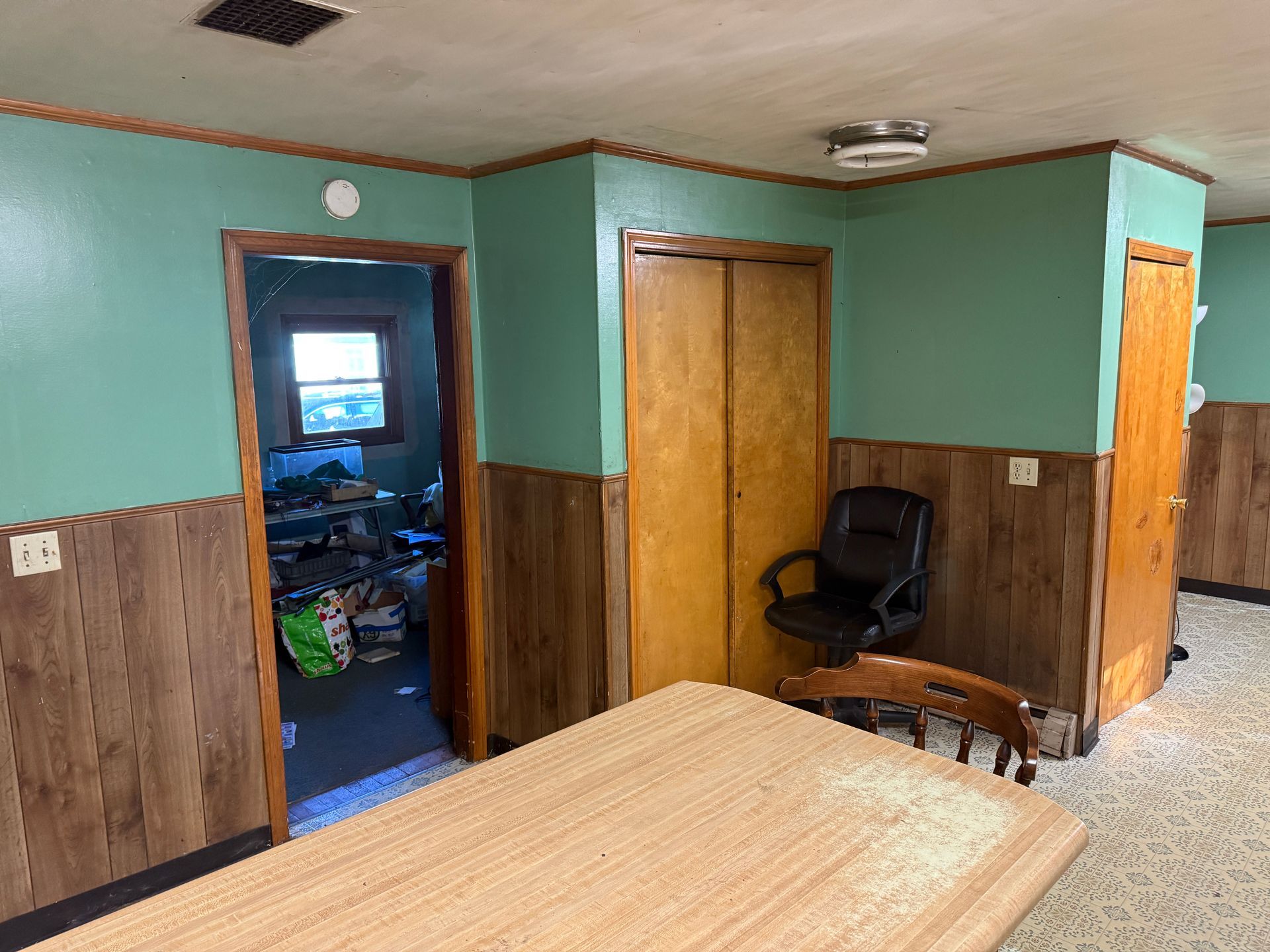Small room with green walls, wood paneling, an open doorway, chairs, and a bed in the foreground.