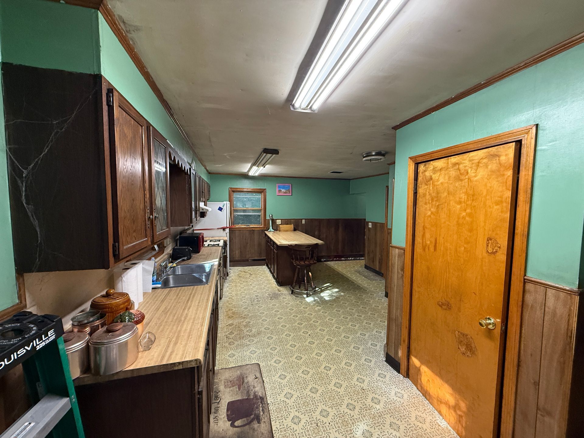 Long narrow kitchen with turquoise walls, wood cabinets, fluorescent lights, and a bright orange door