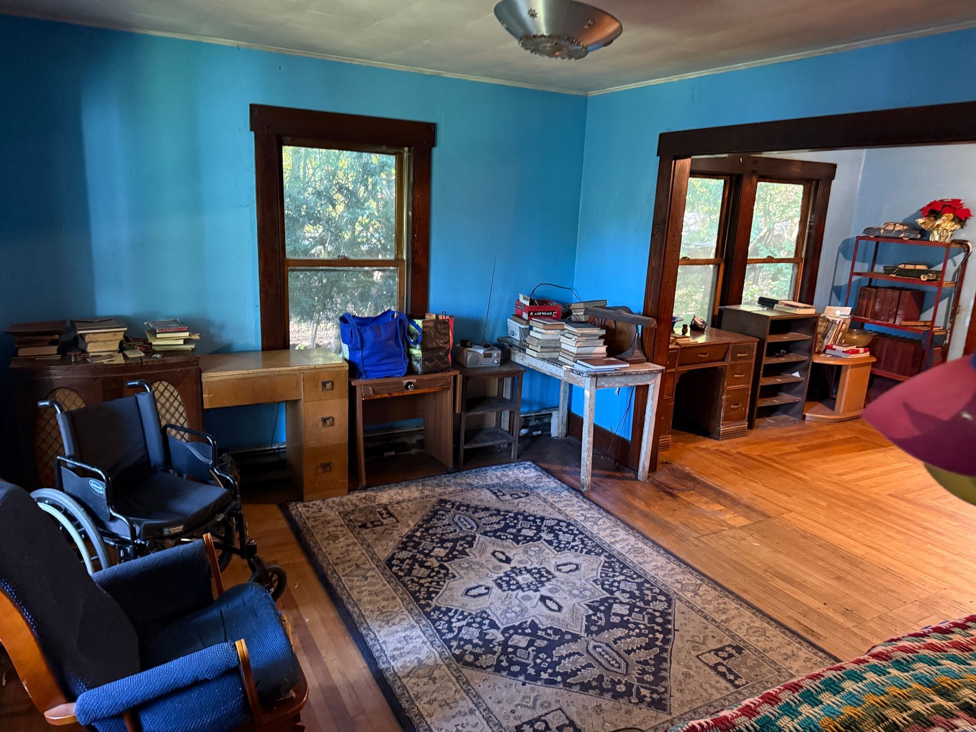Blue room with wooden floor, rug, desk, chairs, and windows letting in daylight