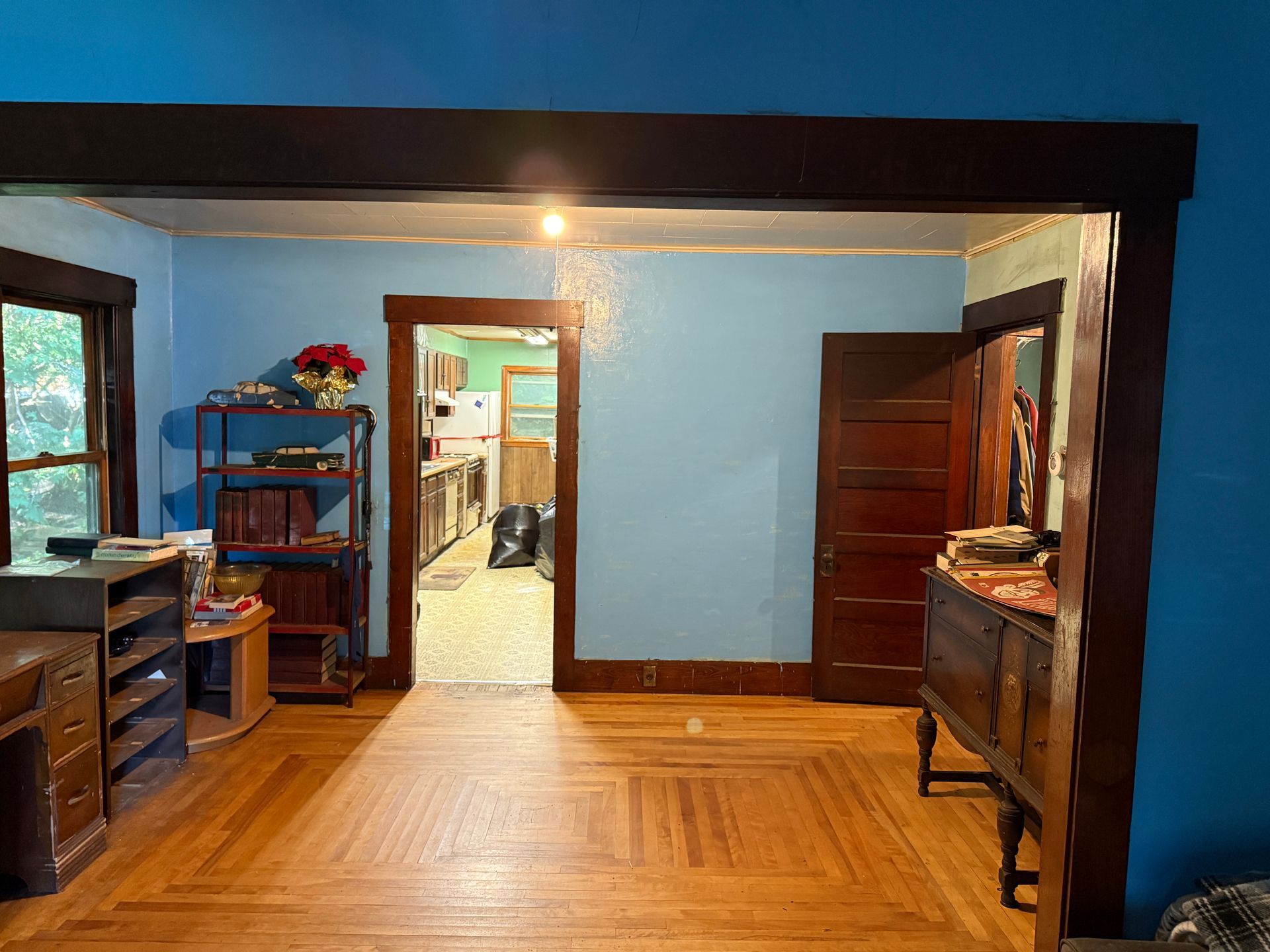 Blue-walled room with wood floor, dark trim, open doorway, and wooden furniture on both sides