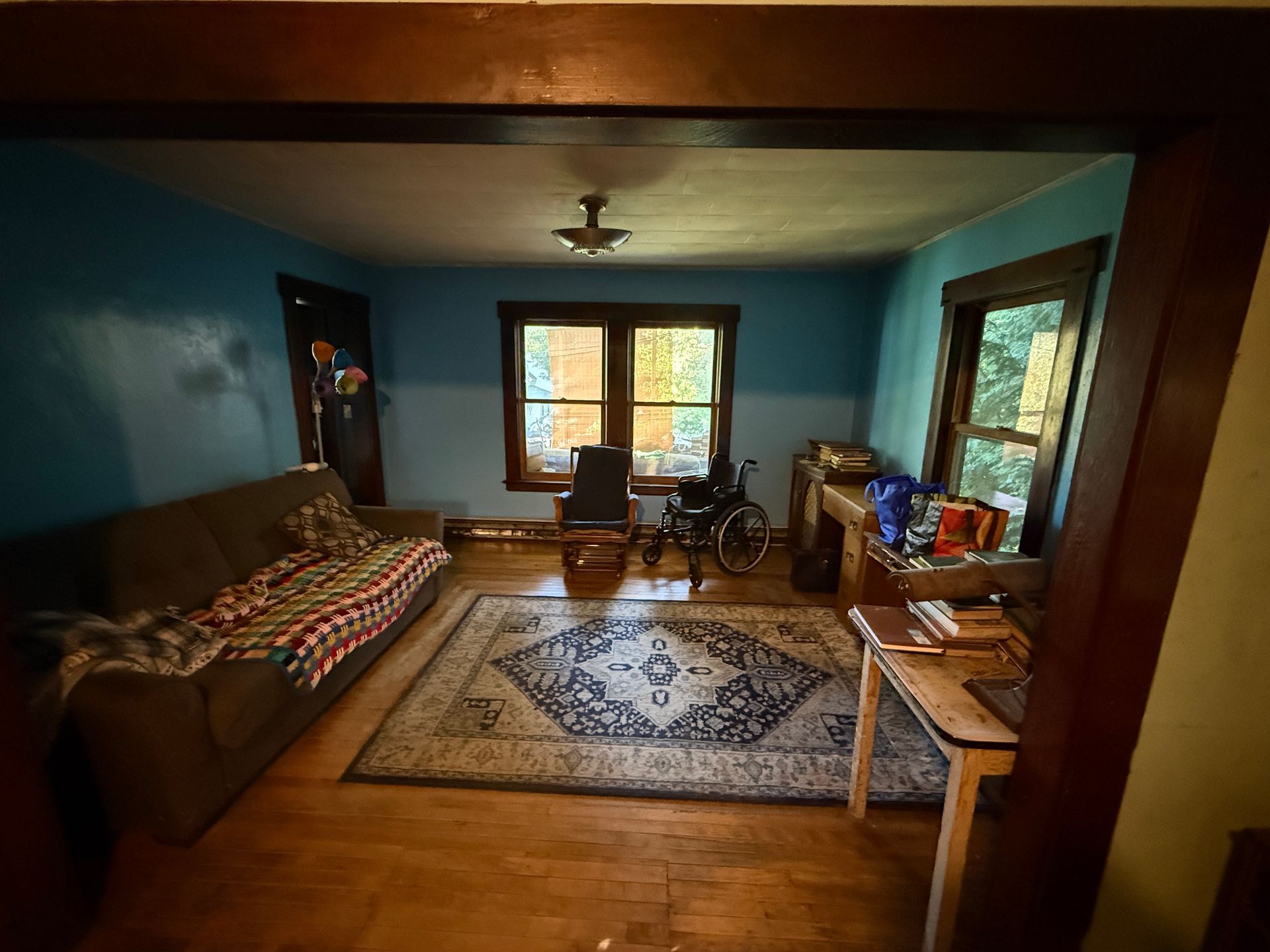 Cozy teal living room with couch, rug, windows, wooden floor, and a small table near the back wall