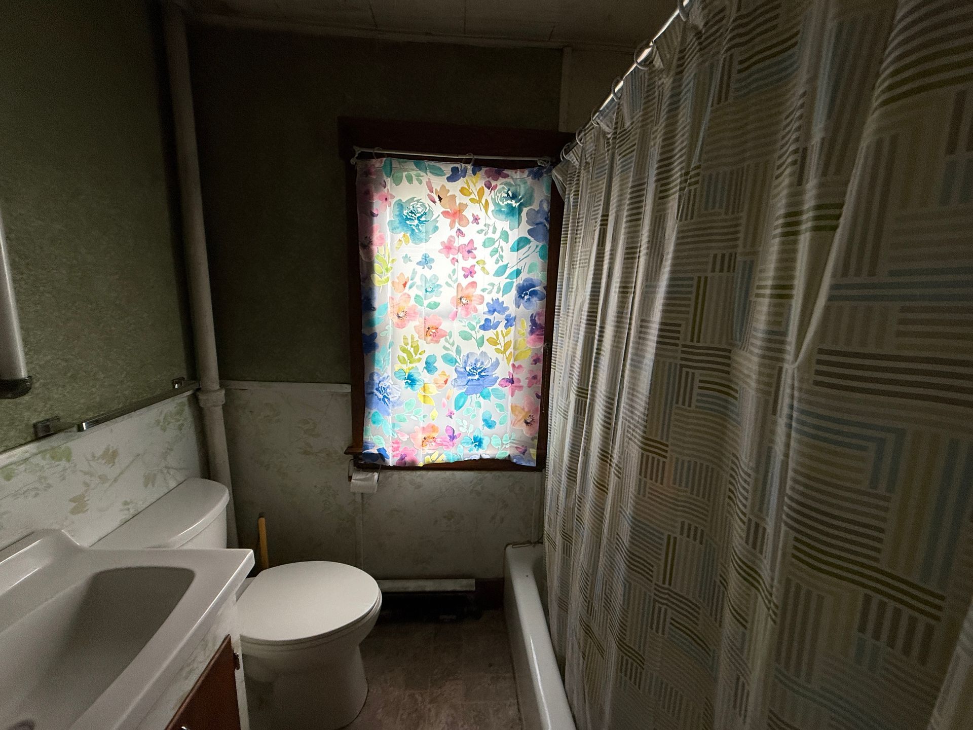 Small bathroom with a sink, toilet, shower curtain, and a colorful patterned window covering.