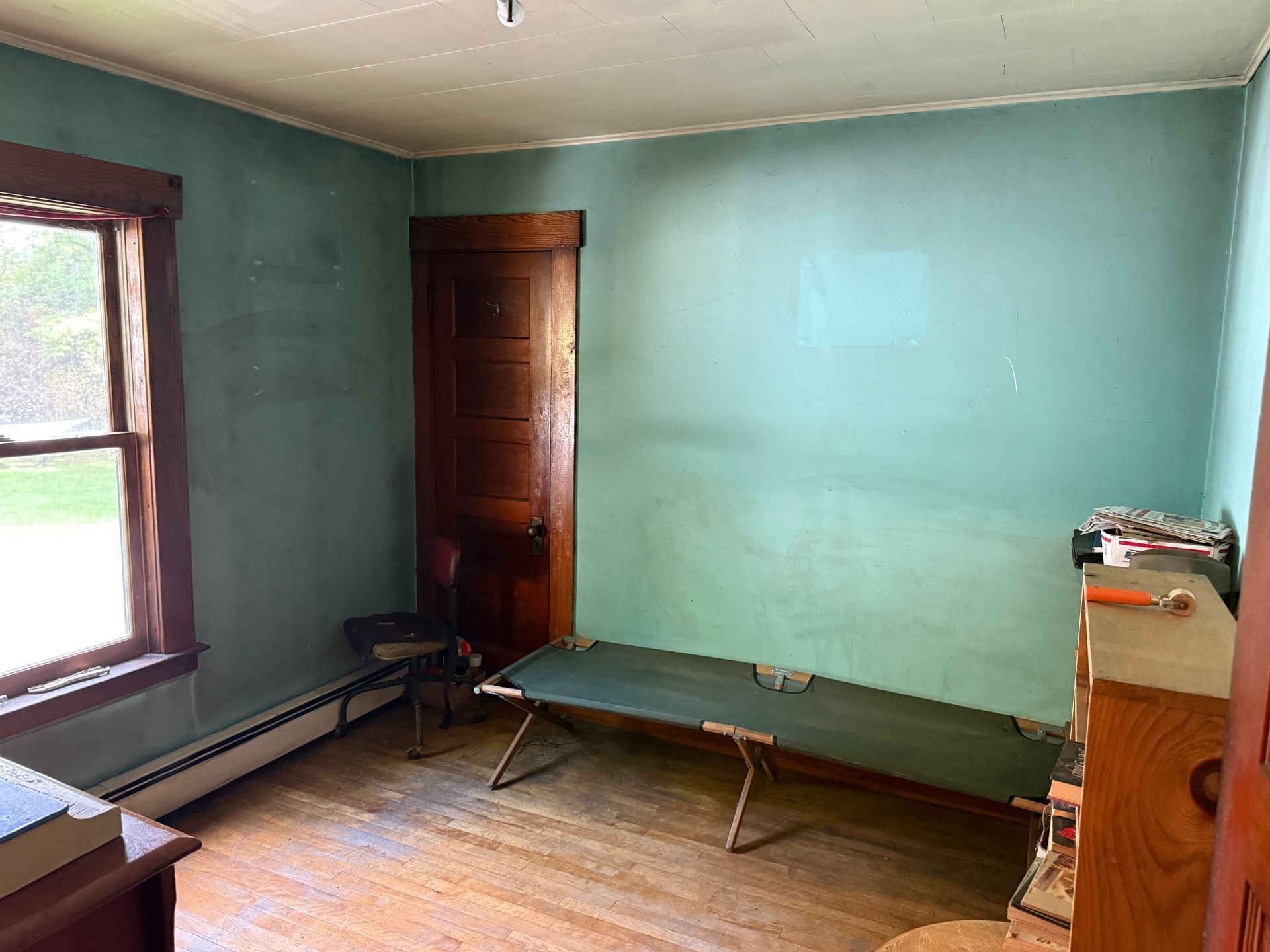 Empty room with mint green walls, two benches, a window, and a wooden door.