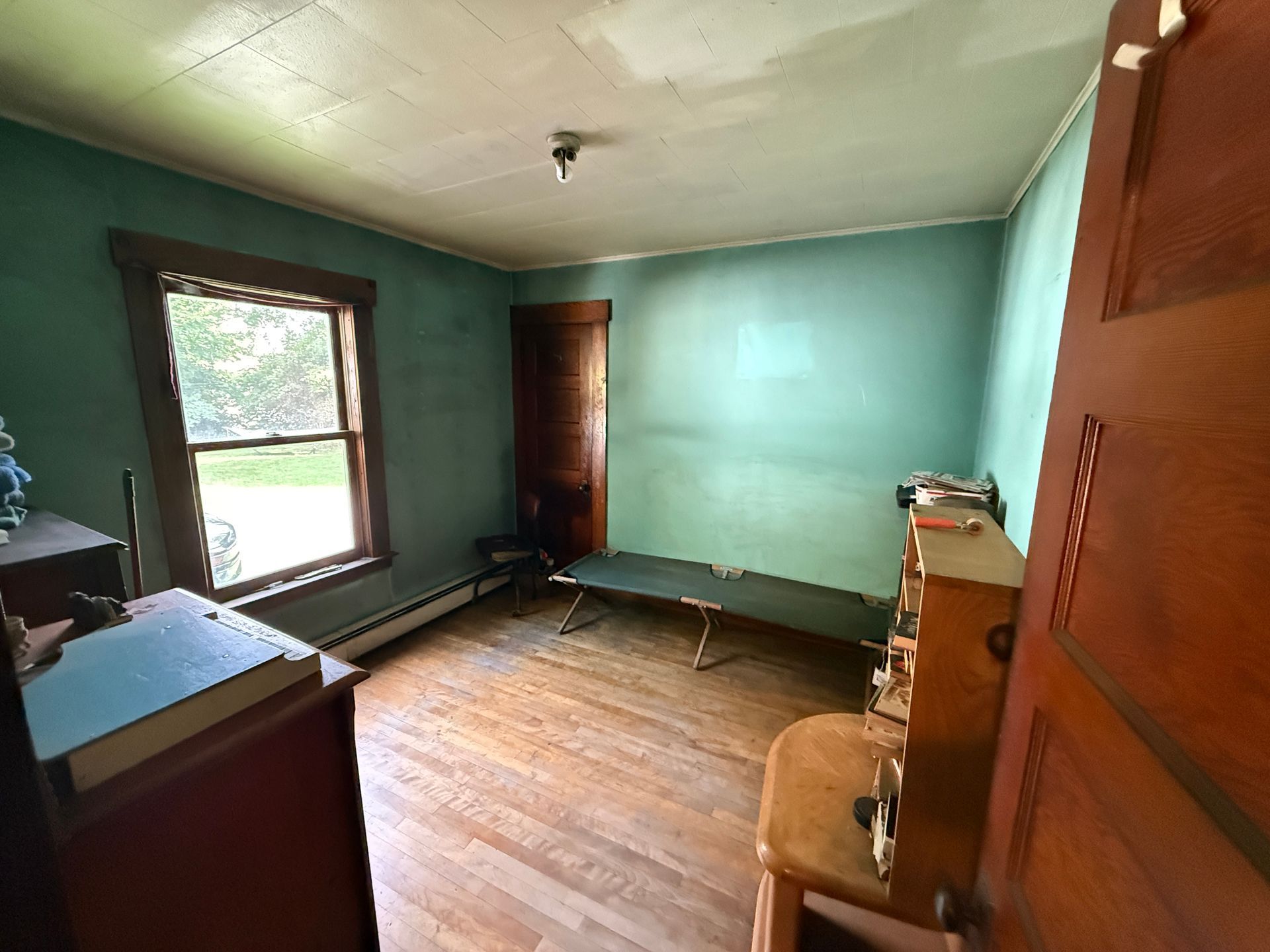 Small empty room with teal walls, wood floor, window, and a dresser by the doorway.