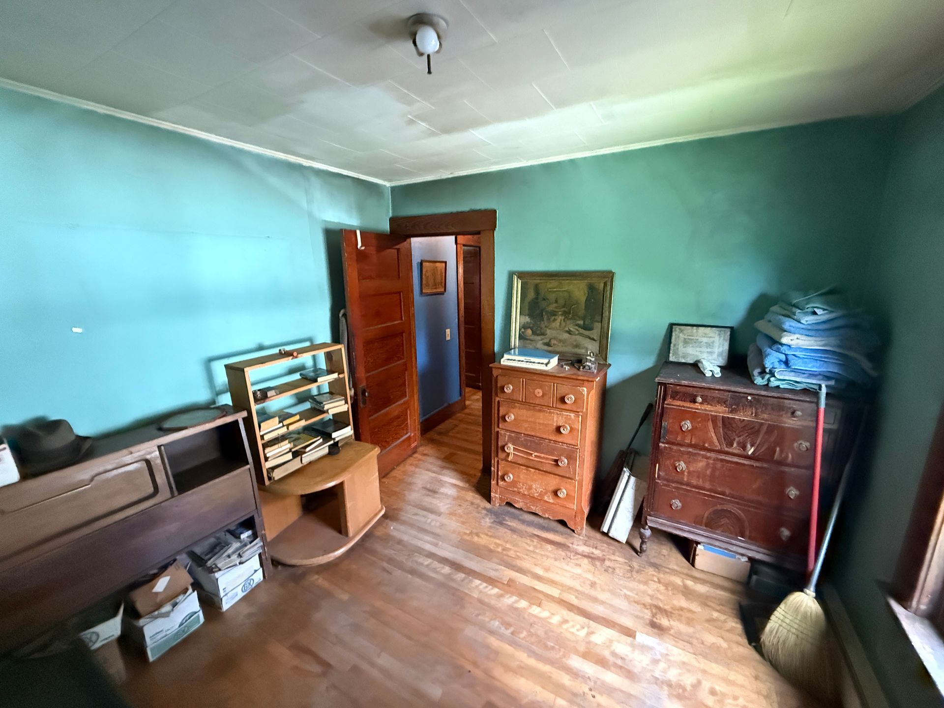 bedroom with teal walls, wooden dressers, a bed, and stacked boxes near an open door